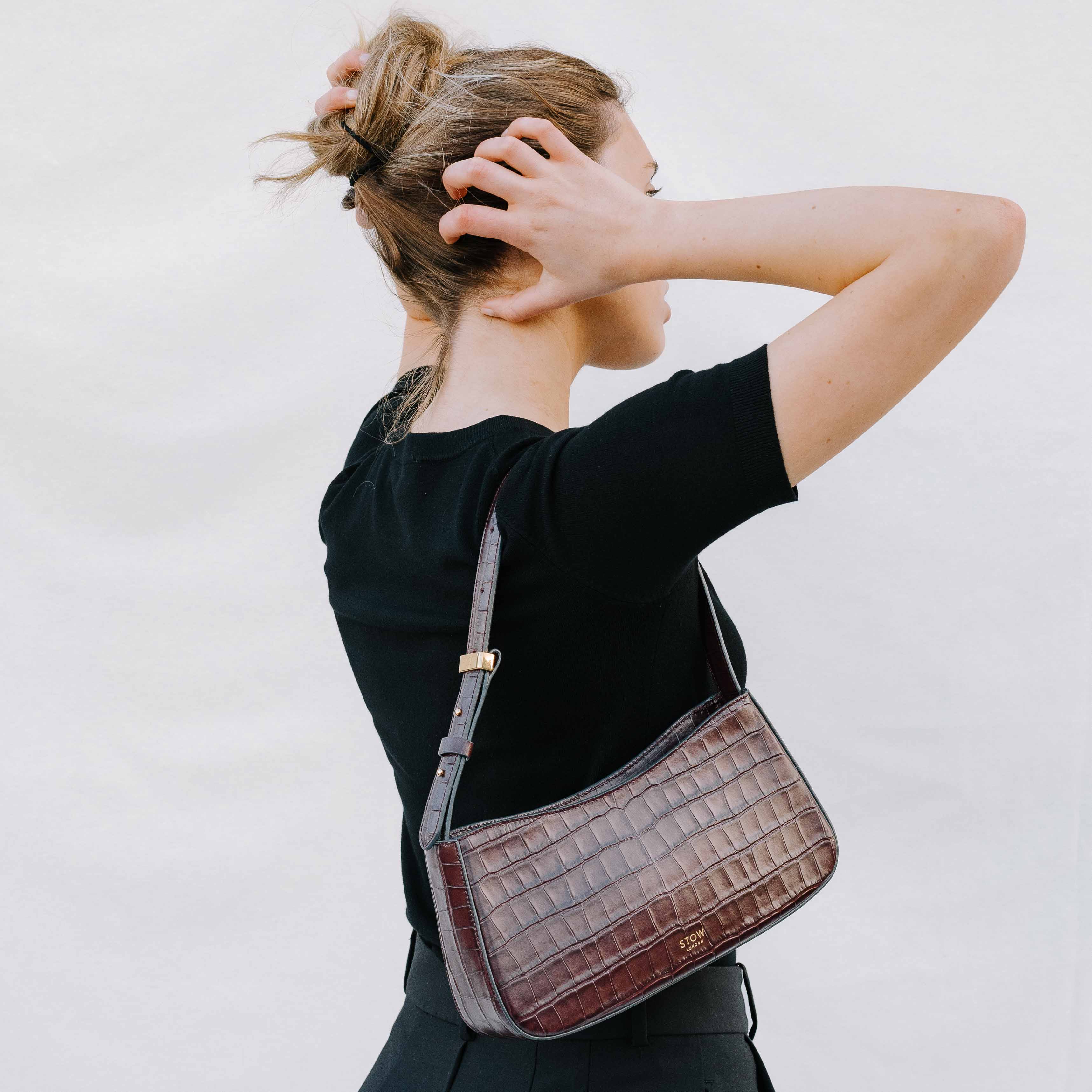 Girl running her hands through her hair with the burgundy embossed croc post shoulder bag on her shoulder on a white background