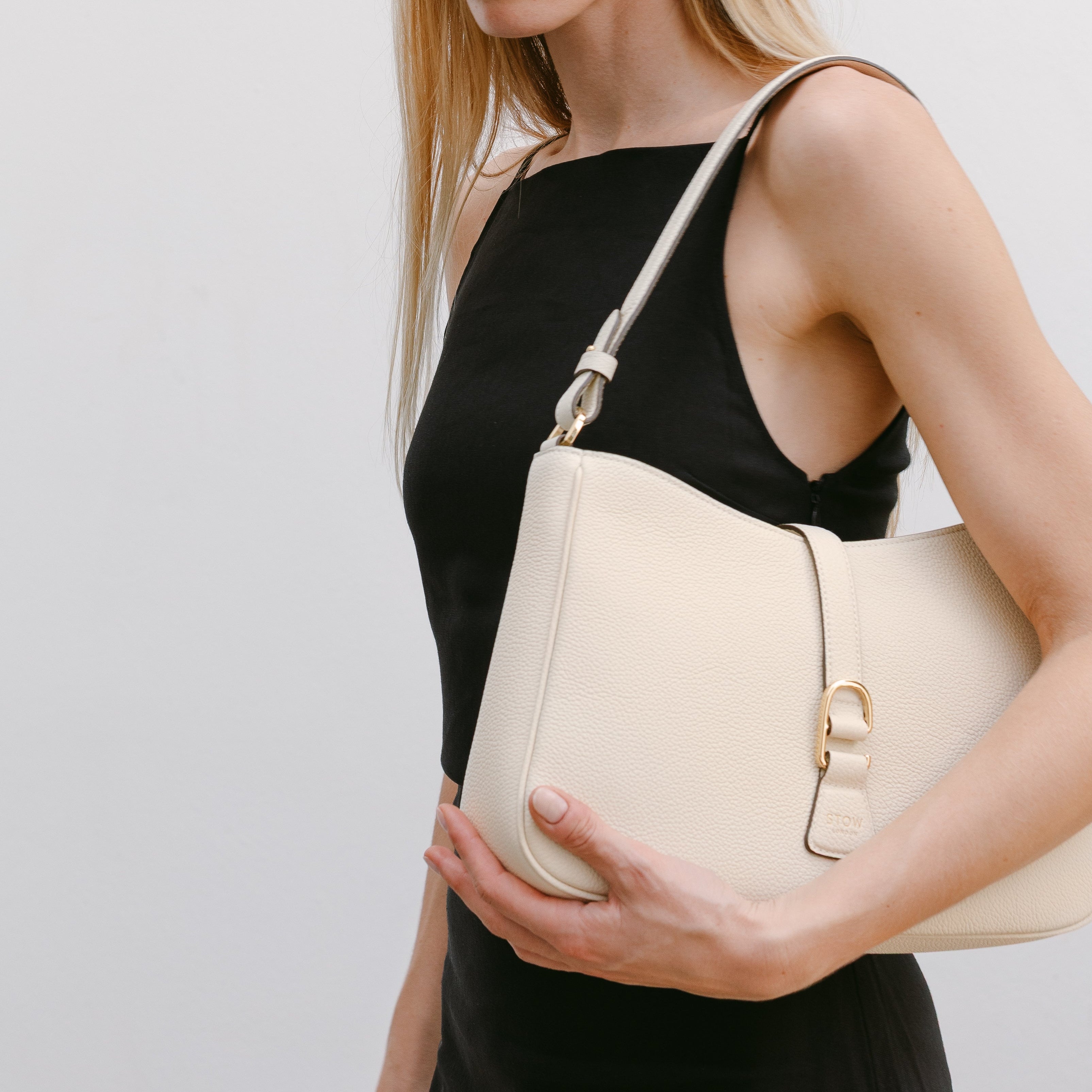 Model wearing STOW London's Beth Shoulder bag in Spring Moon pebbled leather on her shoulder featuring gold-coated stainless steel hardware and clip on a white background