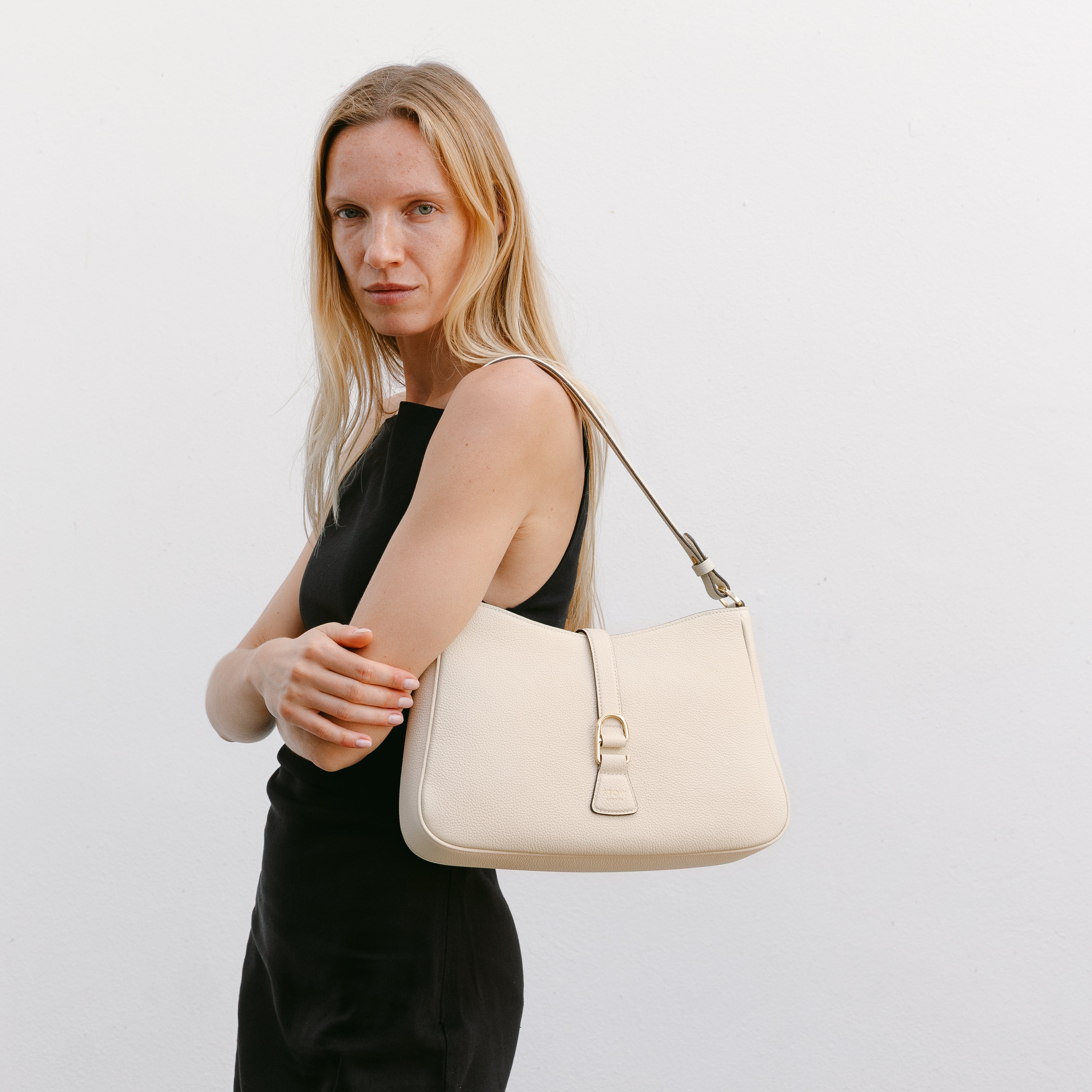Model wearing STOW London's Beth Shoulder bag in Spring Moon pebbled leather on her shoulder featuring gold-coated stainless steel hardware and clip on a white background