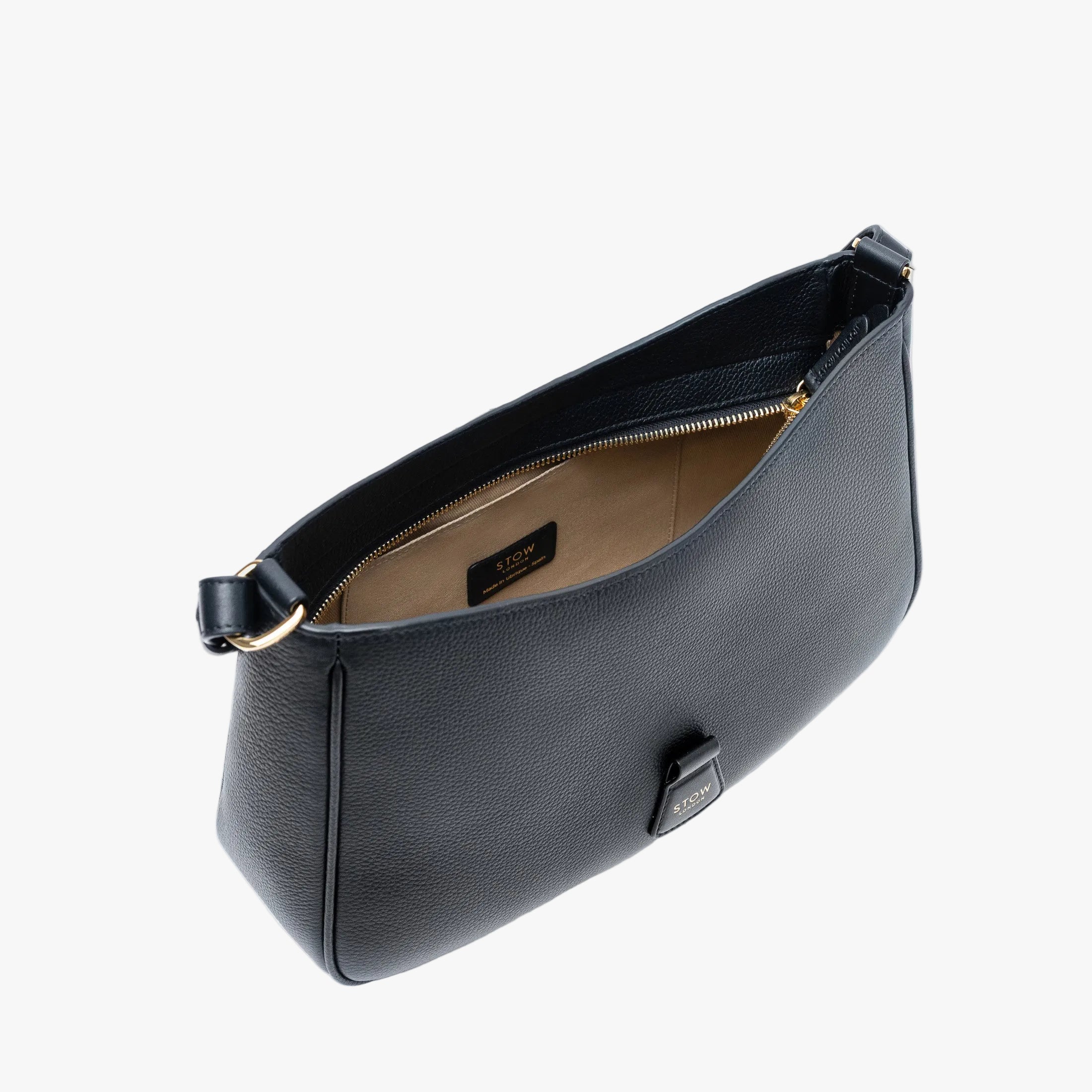 Top angled view of STOW London's Beth bag in Black pebbled and smooth leather with zipper open showing the interior cotton lining and card holder pocket, featuring gold-coated stainless steel hardware on a white background