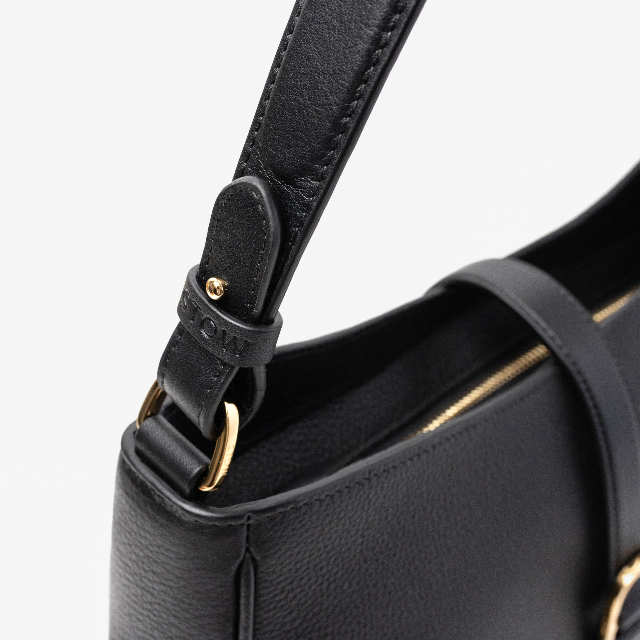 Close up of STOW London's Beth bag in Black pebbled and smooth leather featuring the detachable strap and gold-coated stainless steel hardware on a white background