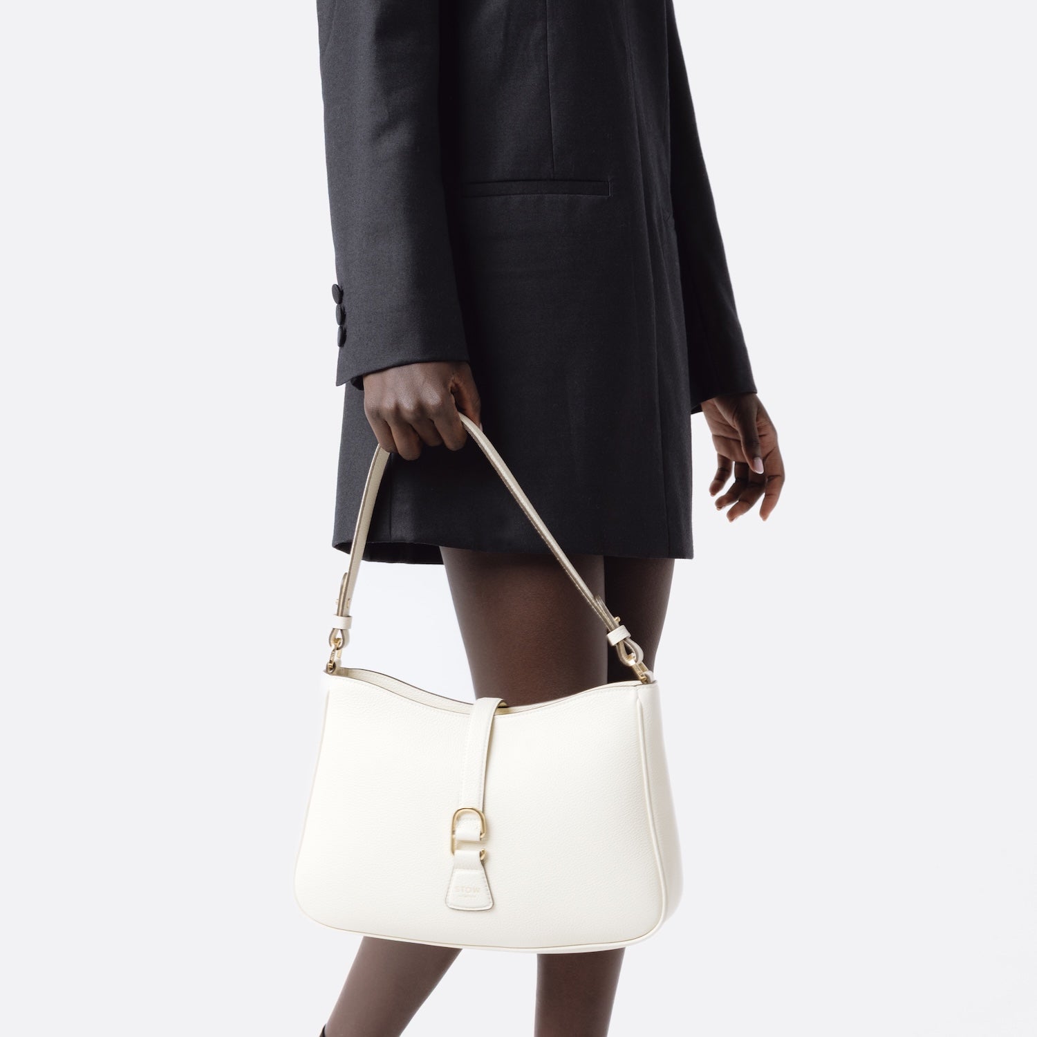 Close shot of model holding STOW London's Beth bag in Spring Moon pebbled and smooth leather at her side featuring gold-coated stainless steel hardware and clip on a white background