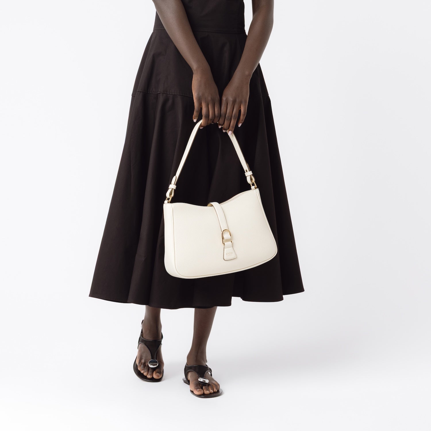 Model holding STOW London's Beth bag in Spring Moon pebbled and smooth leather in her hands at her front featuring gold-coated stainless steel hardware and clip on a white background
