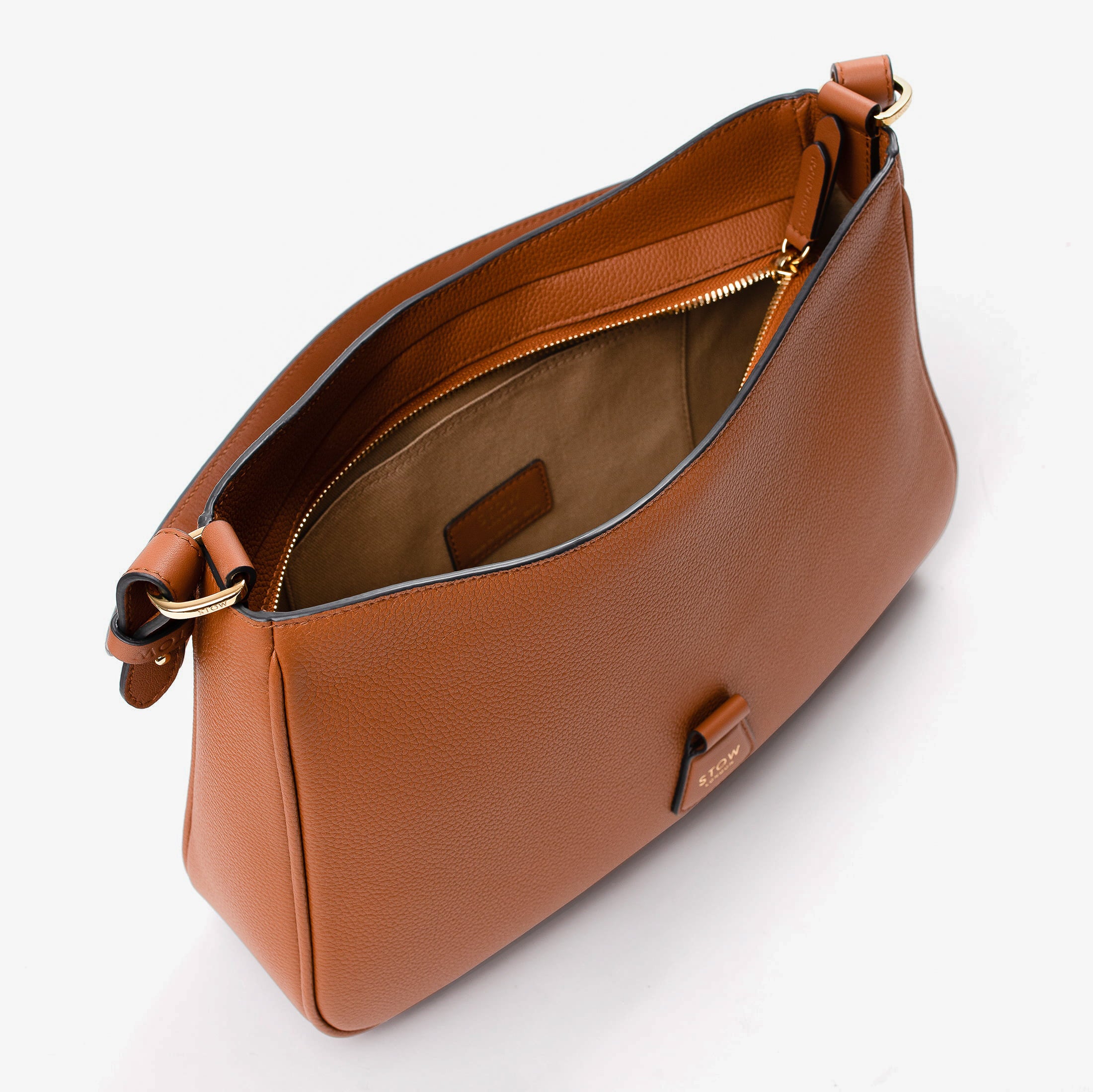 Top angled view of STOW London's Beth bag in Earth Tan pebbled and smooth leather with zipper open showing the interior cotton lining and card holder pocket, featuring gold-coated stainless steel hardware on a white background