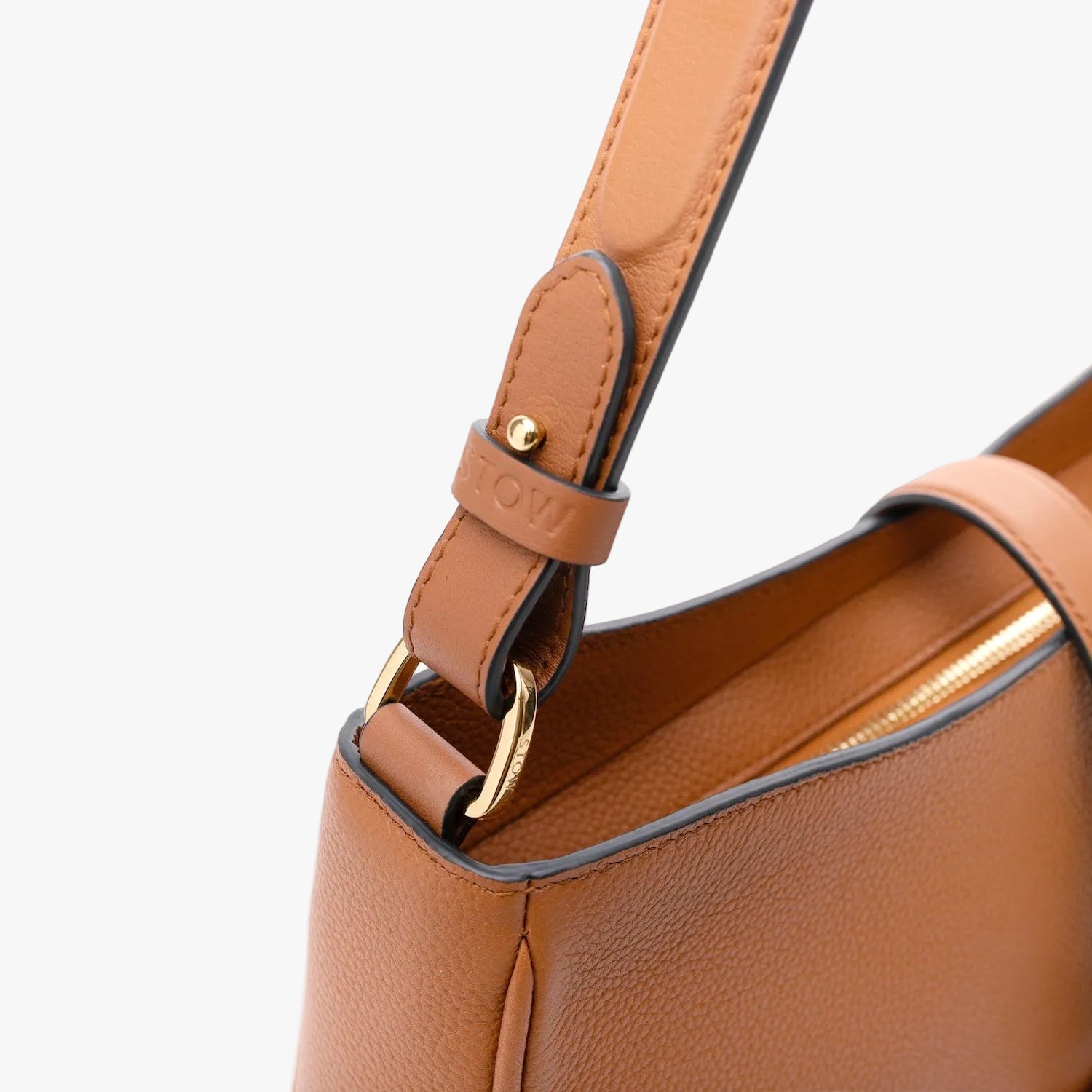 Close up of the strap attachment on STOW London's Beth Shoulder bag in Earth Tan pebbled leather featuring gold-coated stainless steel hardware on a light grey background