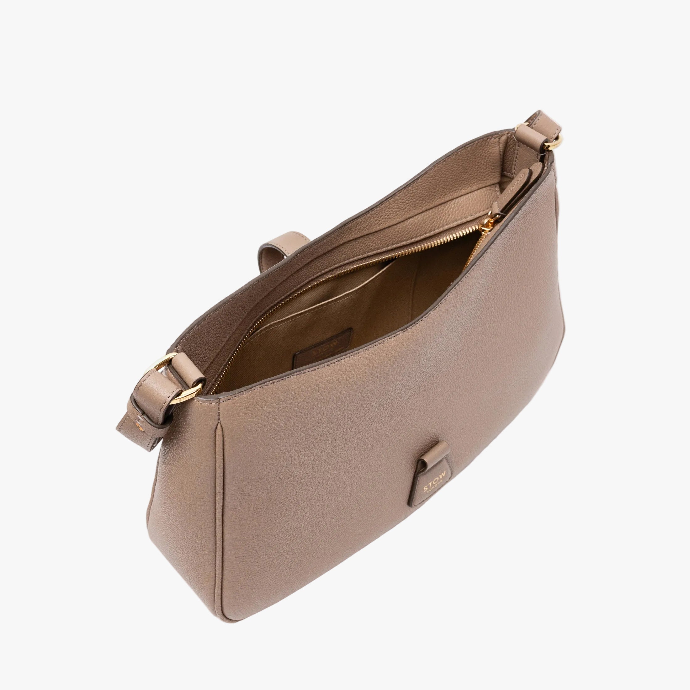 Top angled view of STOW London's Beth bag in Warm Taupe pebbled and smooth leather with zipper open showing the interior cotton lining and card holder pocket, featuring gold-coated stainless steel hardware on a white background