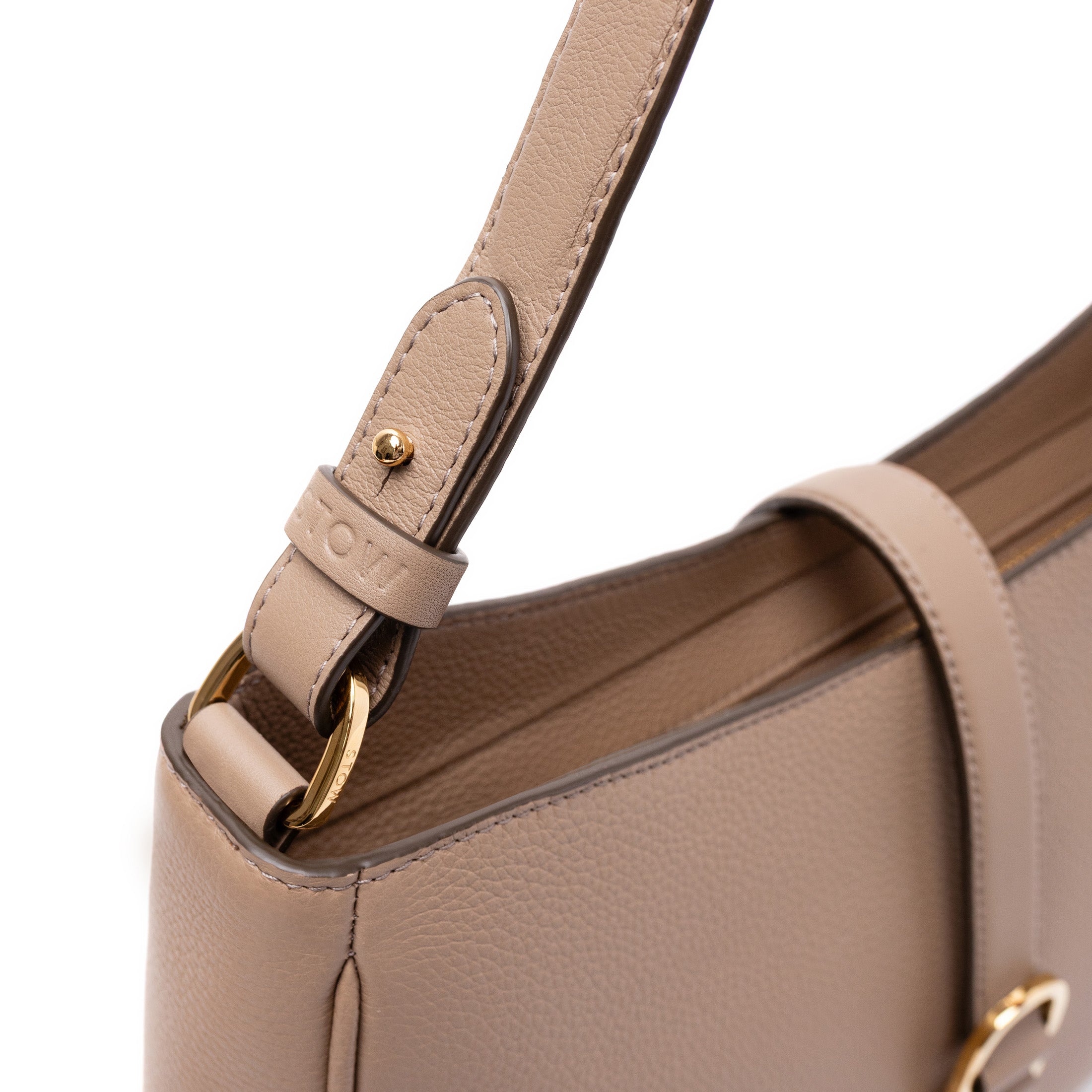 Close up of STOW London's Beth bag in Warm Taupe pebbled and smooth leather featuring the detachable strap and gold-coated stainless steel hardware and clip on a white background