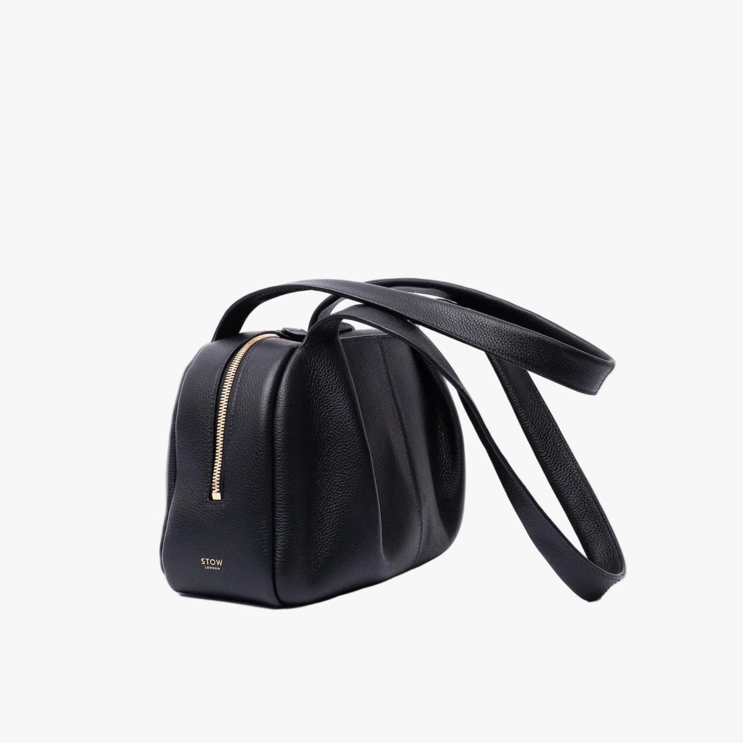 Off-axis view of STOW London's Bowling bag in Black pebbled leather featuring the pleated front panel and gold-coated stainless steel hardware on a light grey background