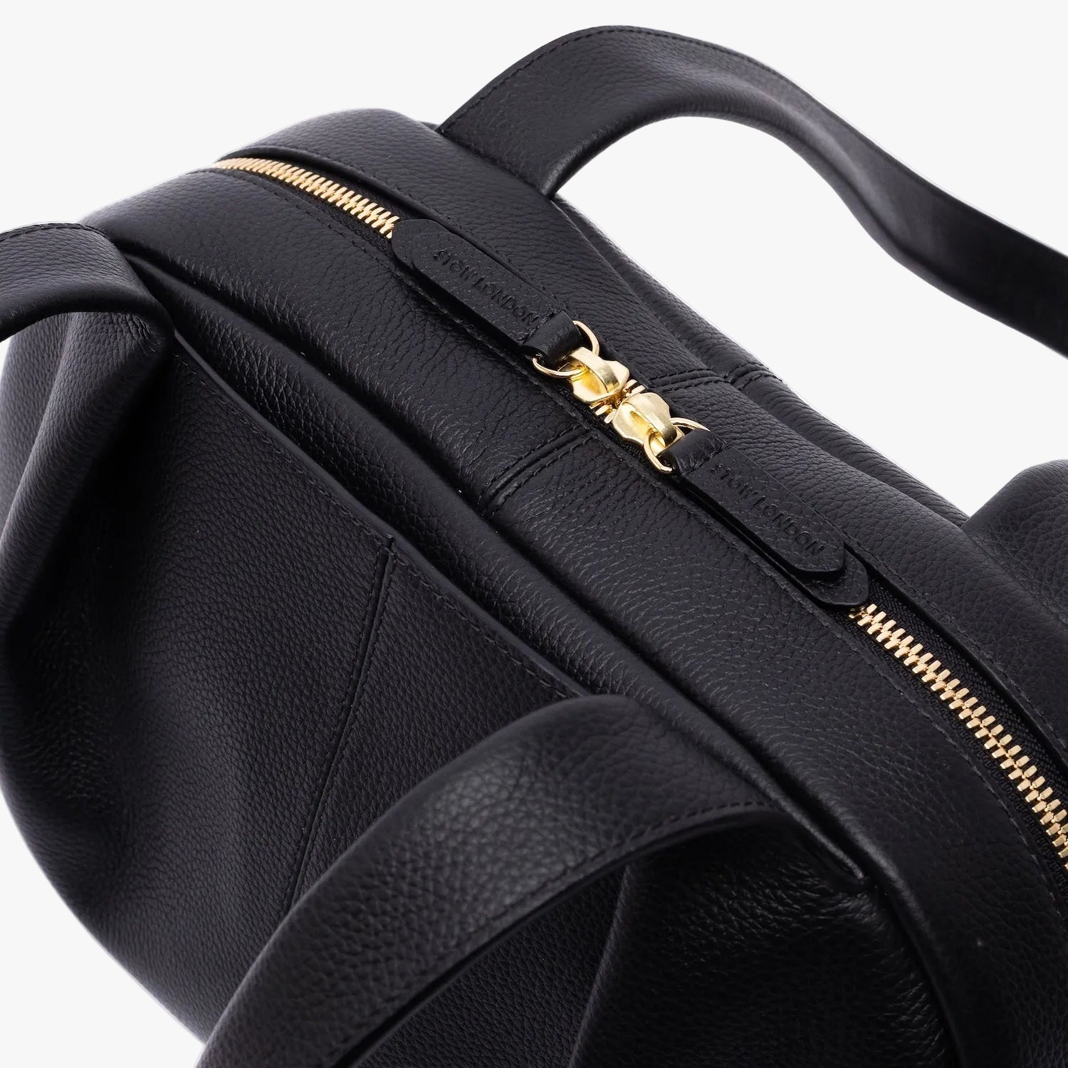 Close up of shot of the gold zip closure of STOW London's Bowling bag in Black pebbled leather on a light grey background
