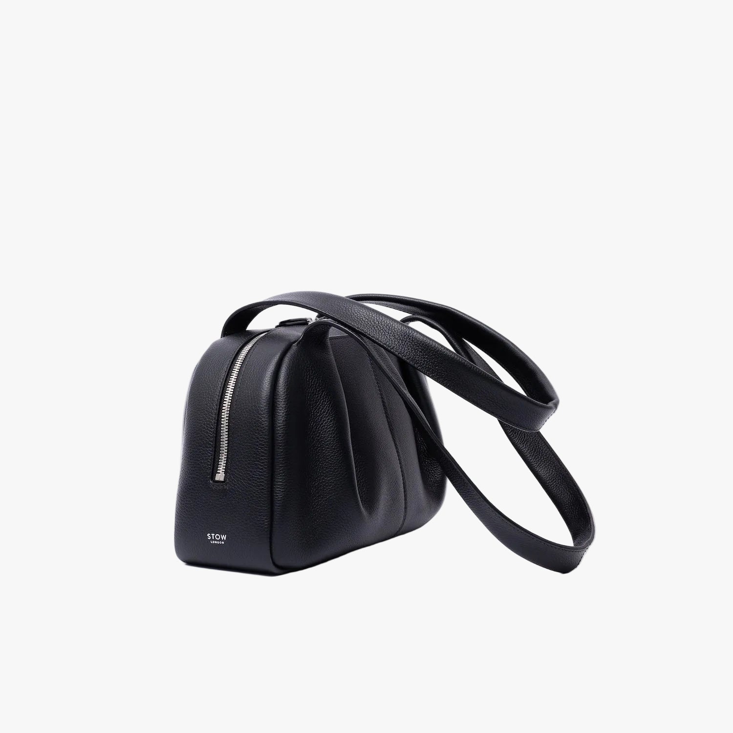 Off-axis view of STOW London's Bowling bag in Black pebbled leather featuring the pleated front panel and silver stainless steel hardware on a light grey background