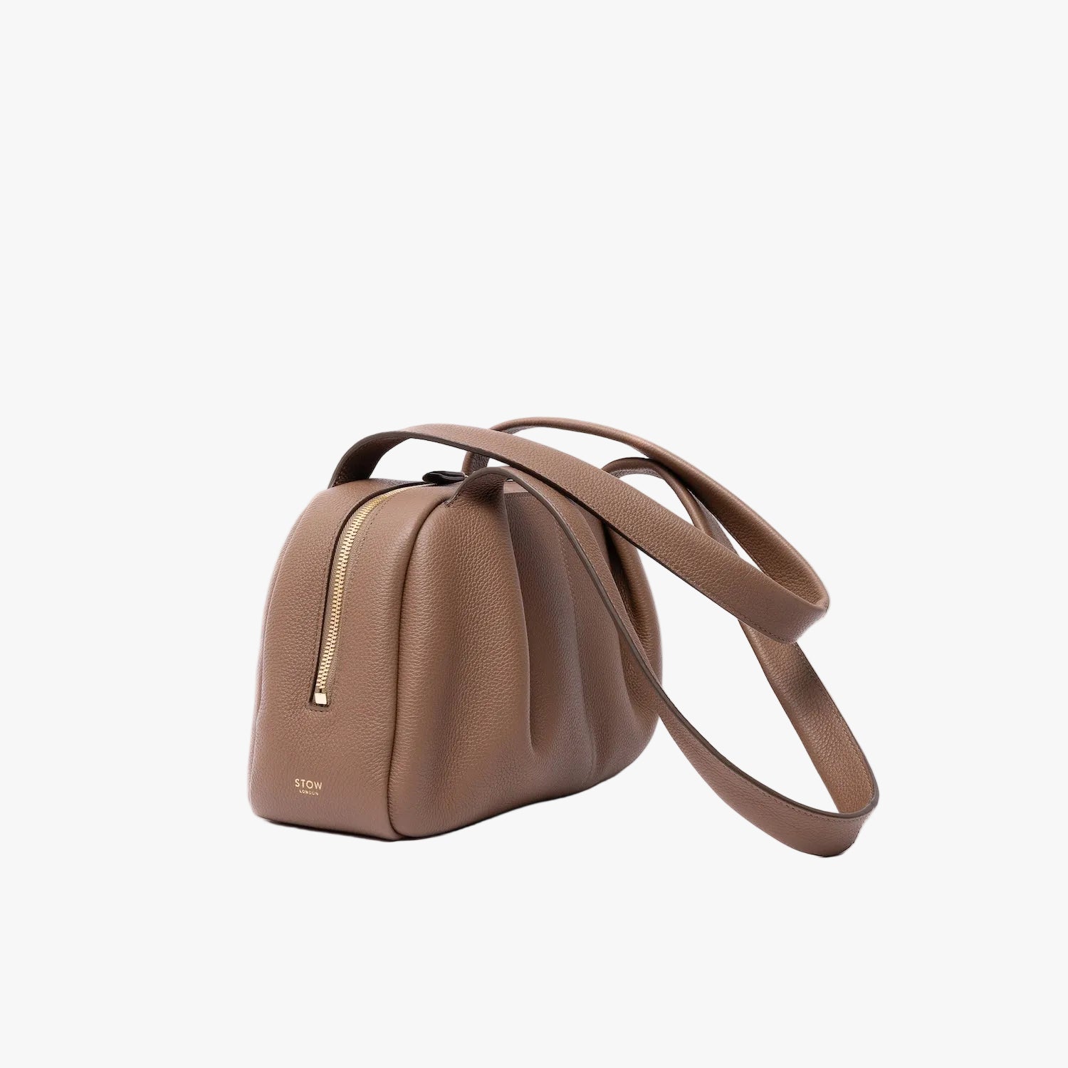 Off-axis view of STOW London's Bowling bag in Mocha pebbled leather featuring the pleated front panel and gold-coated stainless steel hardware on a light grey background