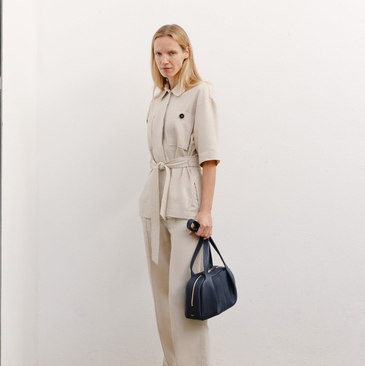 Model with STOW London's Bowling bag in Navy pebbled leather featuring the pleated front panel and gold-coated stainless steel hardware