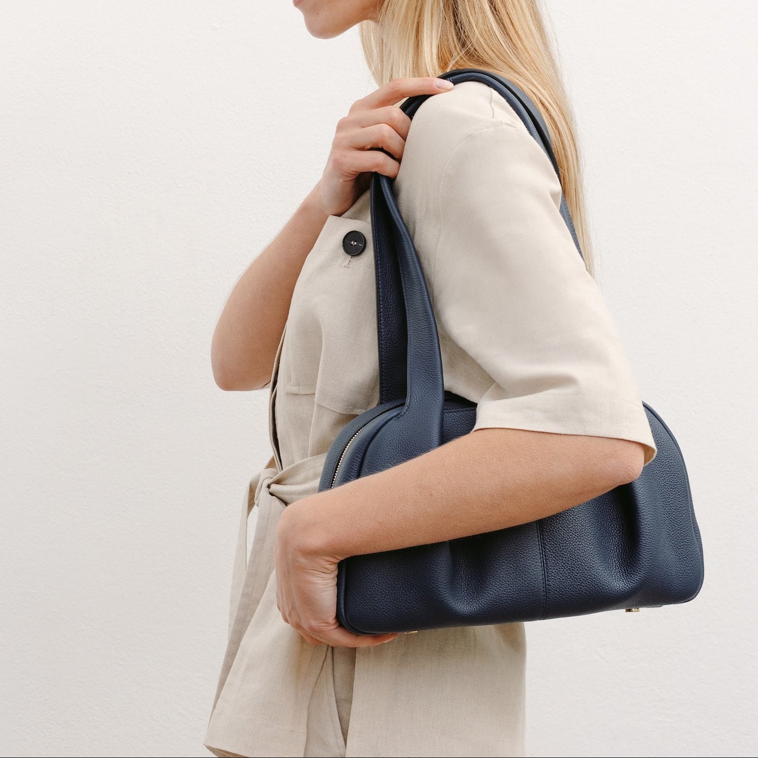 Model wearing STOW London's Bowling bag in Navy pebbled leather on her shoulder featuring the pleated front panel and gold-coated stainless steel hardware