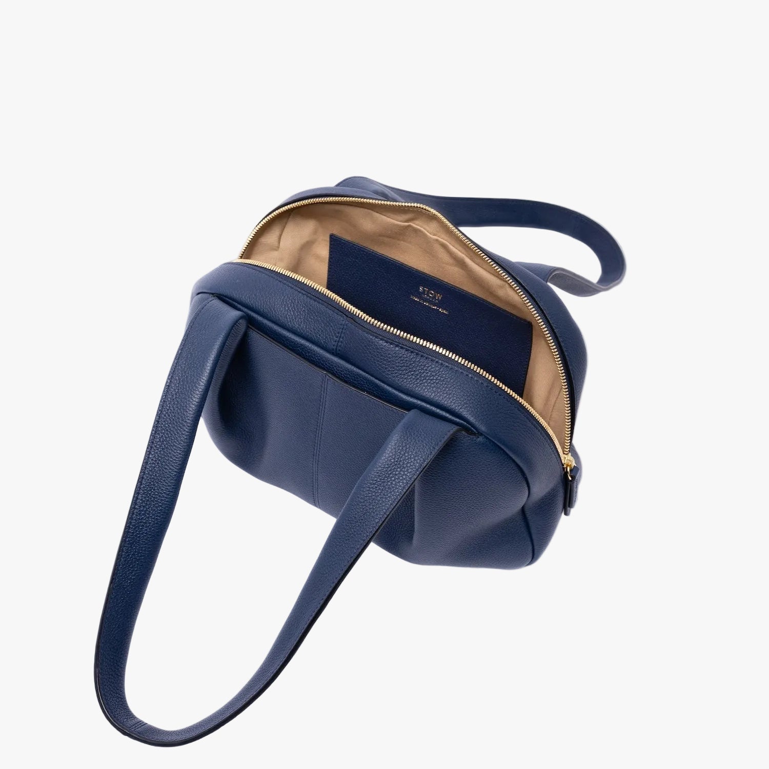 Top view of STOW London's Bowling bag in Navy pebbled leather on a light grey background with zip open showing the interior cotton lining and leather slip pocket