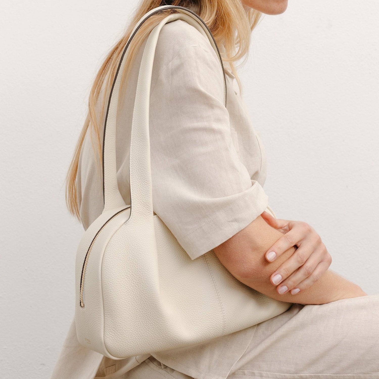 Model wearing STOW London's Bowling bag in Spring Moon pebbled leather featuring the pleated front panel and gold-coated stainless steel hardware
