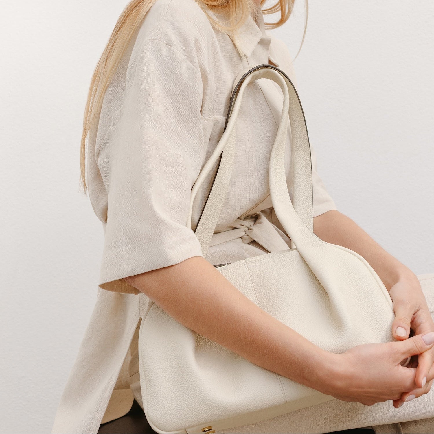 Model holding STOW London's Bowling bag in Spring Moon pebbled leather featuring the pleated front panel and gold-coated stainless steel hardware