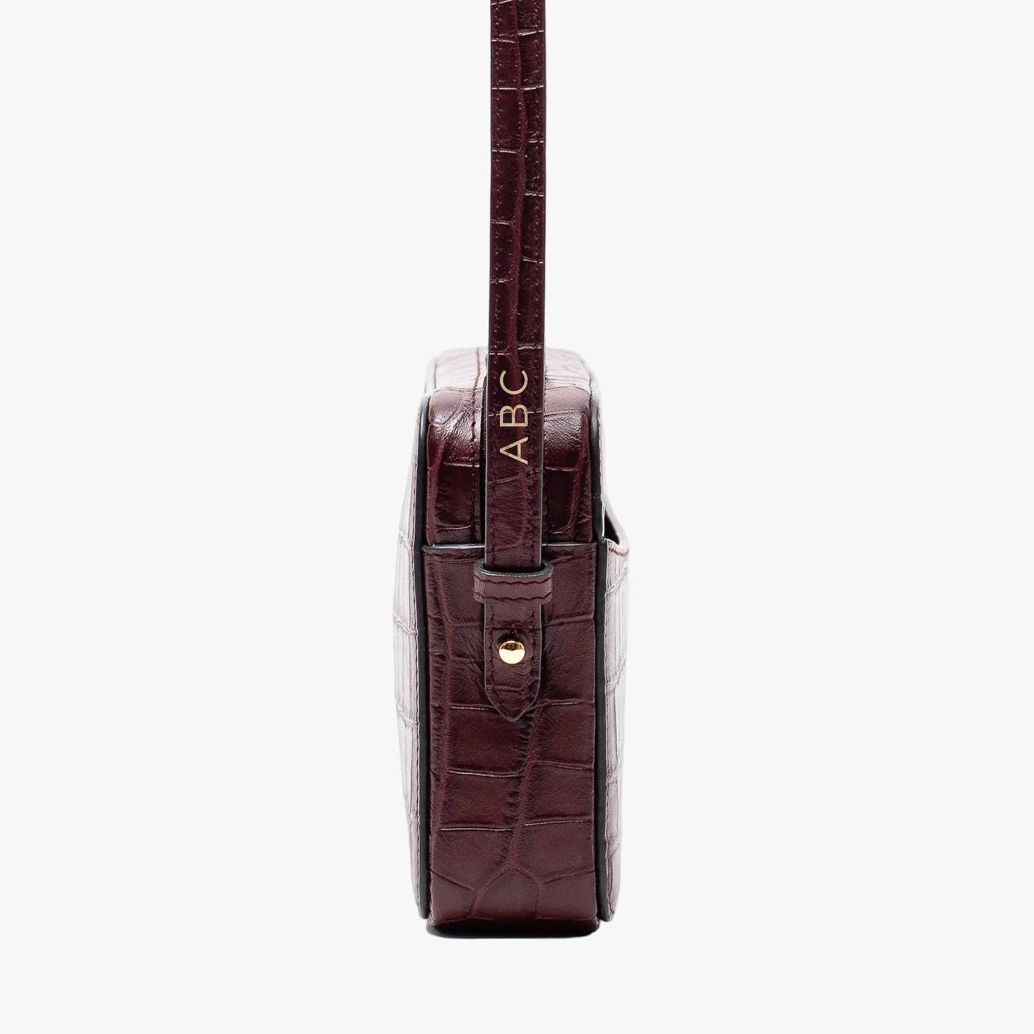 Side view of STOW London's Camera bag in Burgundy Embossed Croc leather showcasing the personalisation positioning and featuring gold-coated stainless steel hardware on a white background