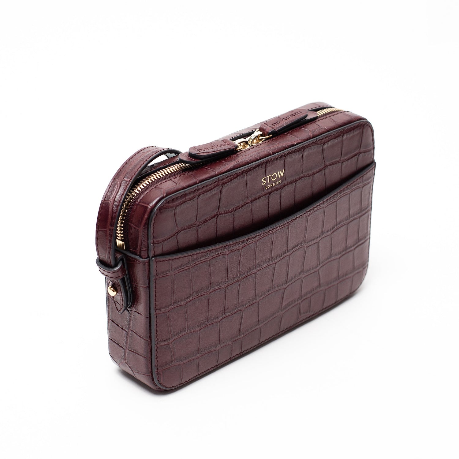 Off-axis view of STOW London's Camera bag in Burgundy Embossed Croc leather featuring gold-coated stainless steel hardware on a white background