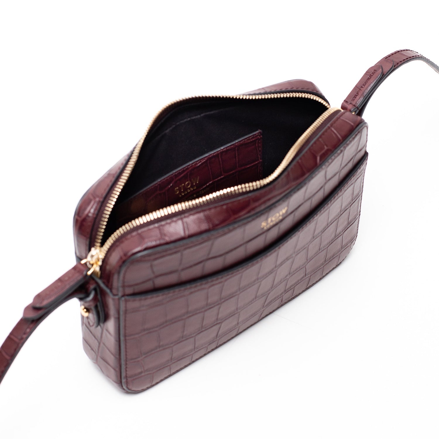Top angled view of STOW London's Camera bag in Burgundy Embossed Croc leather with zipper open showing interior card holder pocket featuring gold-coated stainless steel hardware on a white background