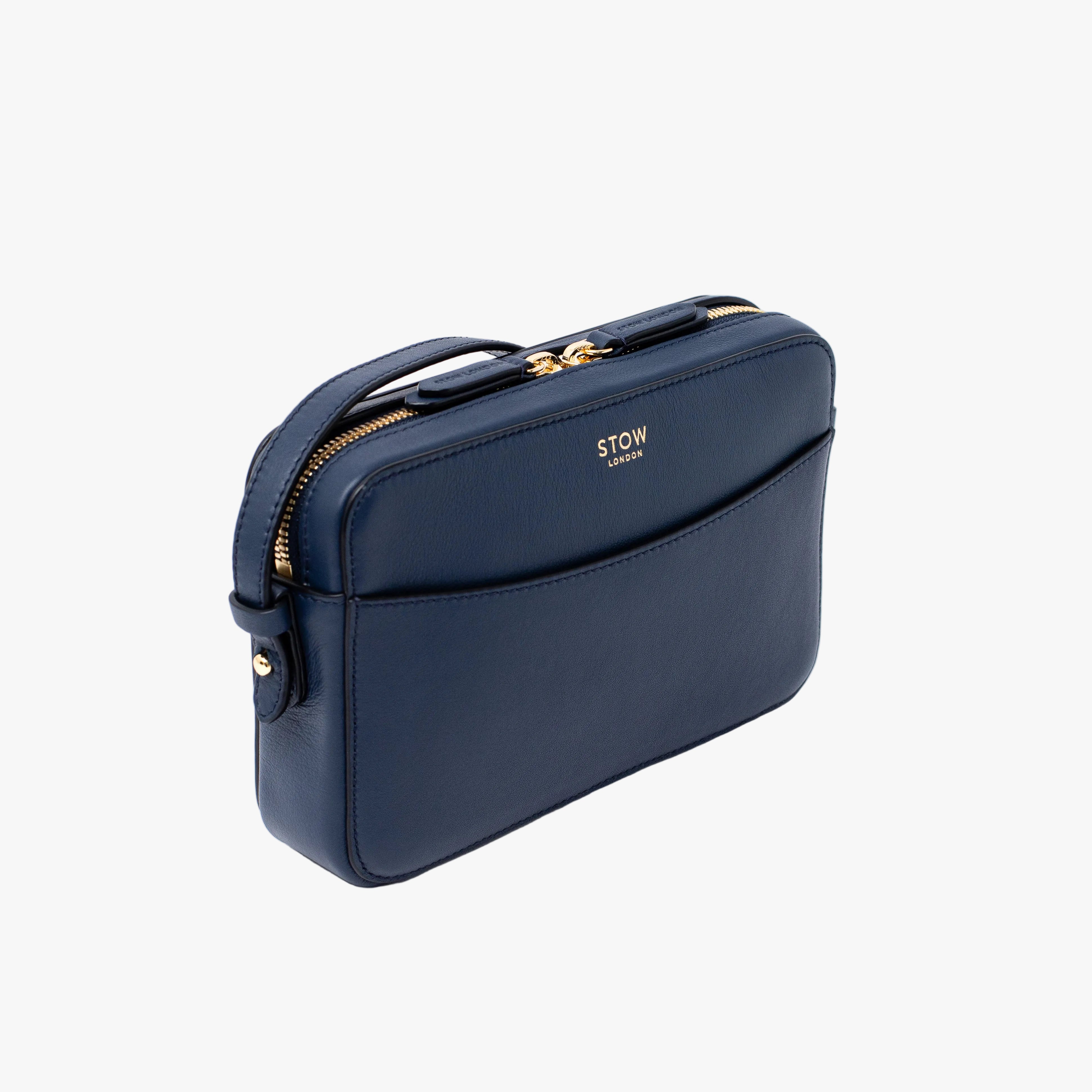 Off-axis view of STOW London's Camera bag in Navy Smooth leather featuring gold-coated stainless steel hardware on a white background