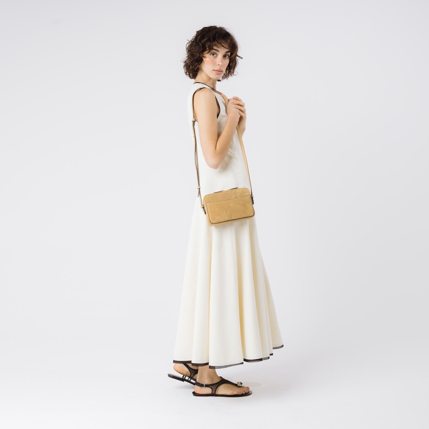 Model wearing STOW London's Camera bag in Soft Sand Suede leather on her shoulder with adjustable strap featuring gold-coated stainless steel hardware on a white background