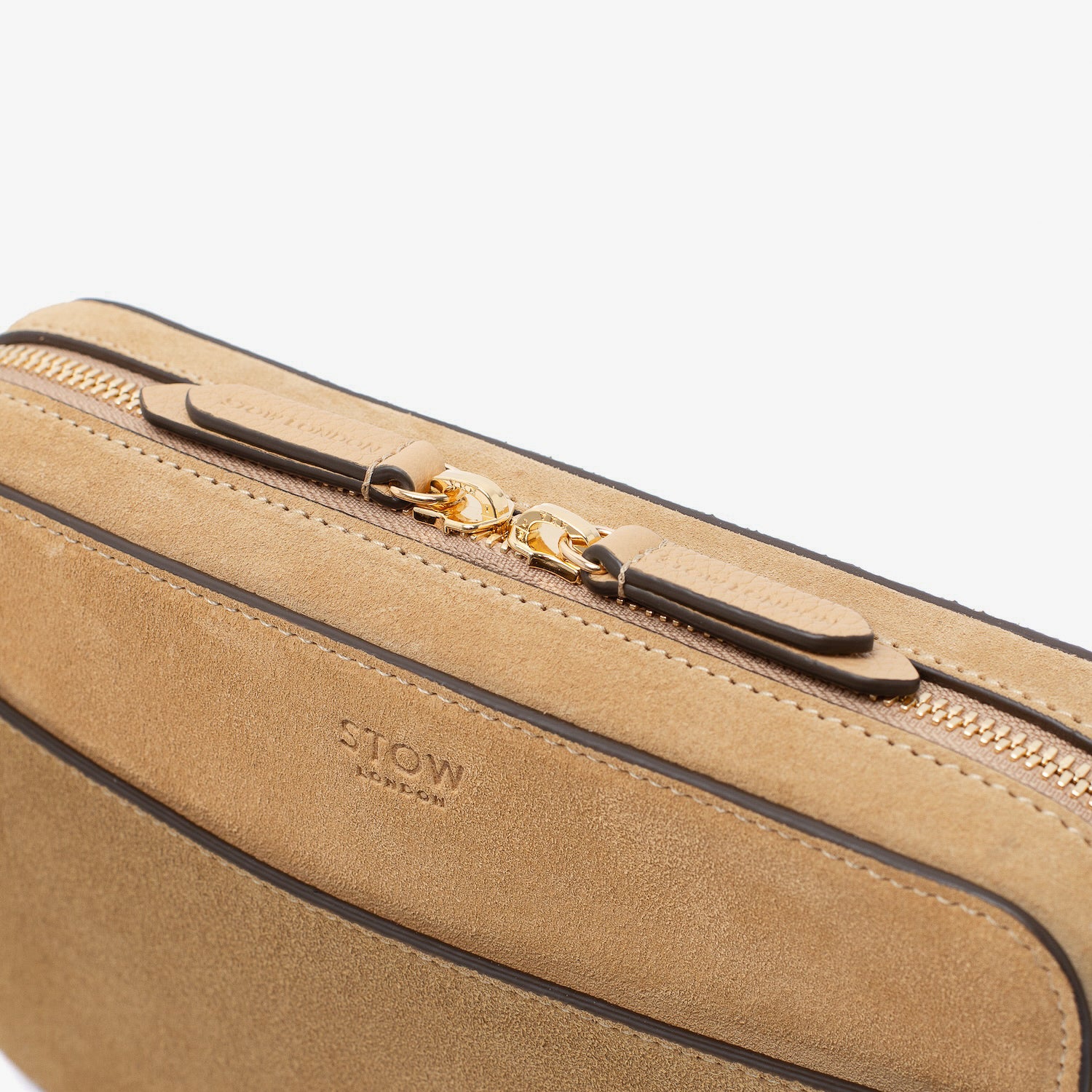 Close up of zip and brand engraved pull tabs on STOW London's Camera bag in Soft Sand Suede leather featuring gold-coated stainless steel hardware on a white background