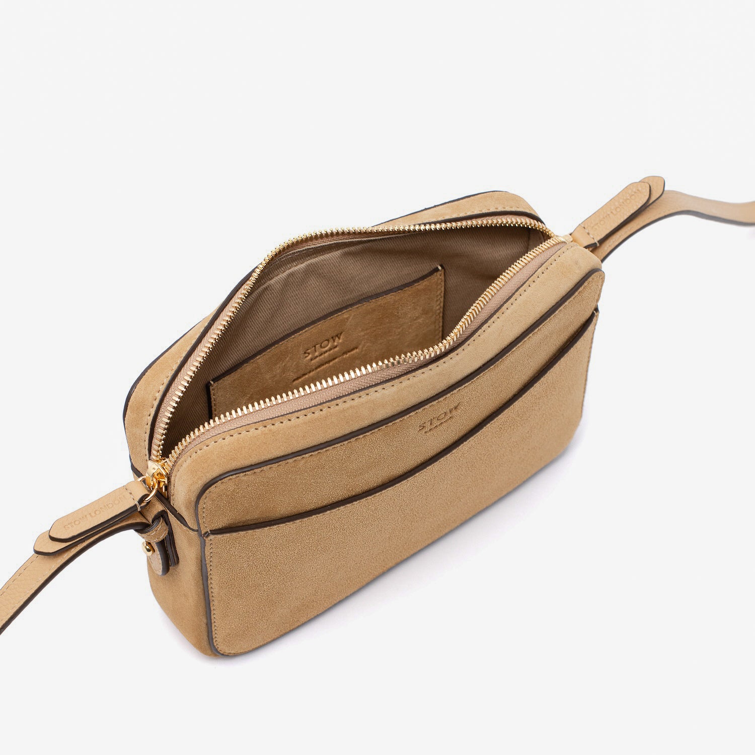 Top view of STOW London's Camera bag in Soft Sand suede leather with zip open showing the bag's interior featuring gold-coated stainless steel hardware on a white background