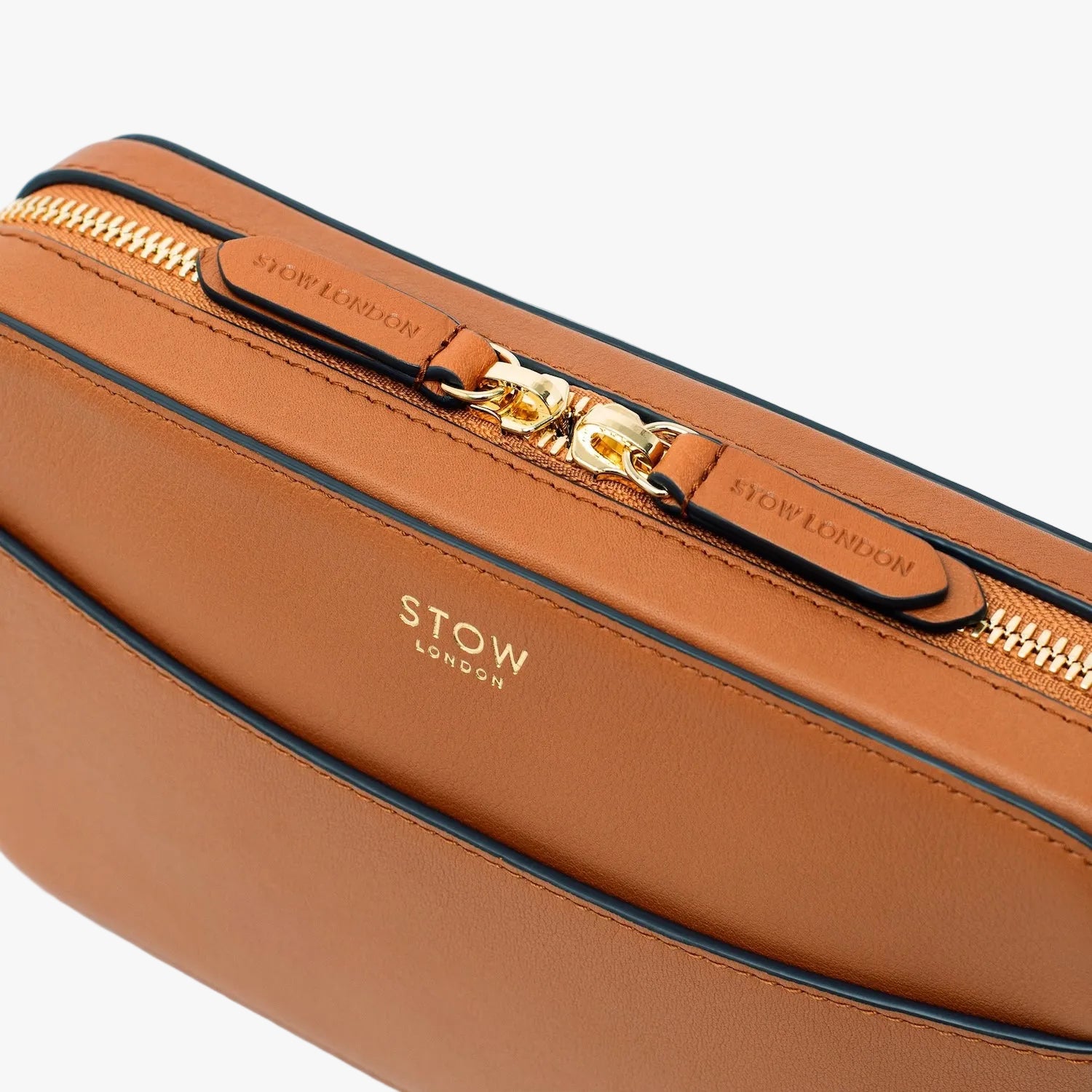 Close up of the top of STOW London's Camera bag in Earth Tan pebbled leather featuring the zip closure and gold-coated stainless steel hardware on a light grey background