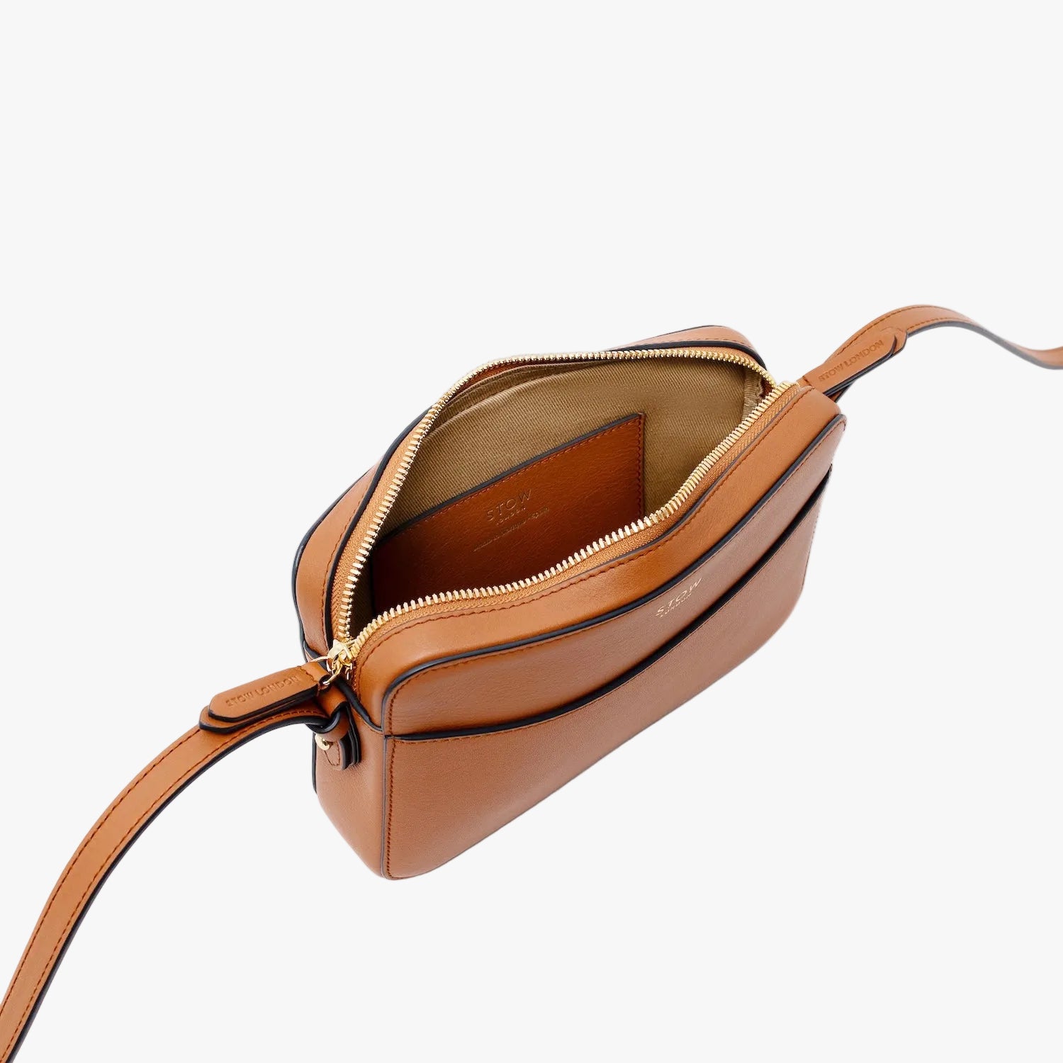 Top angled view of STOW London's Camera bag in Earth Tan Smooth leather with zipper open showing the interior card holder pocket featuring gold-coated stainless steel hardware on a light grey background