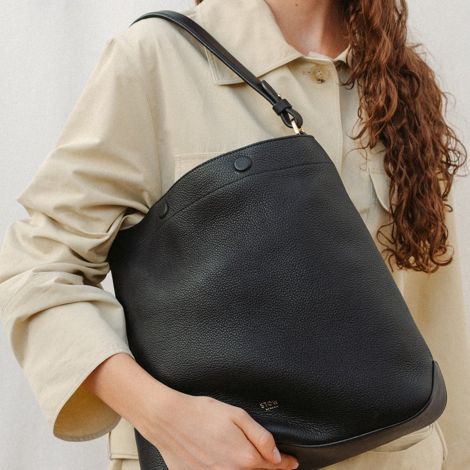 Model holding STOW London's Curve in Black leather featuring the detachable shoulder strap with gold hardware and details