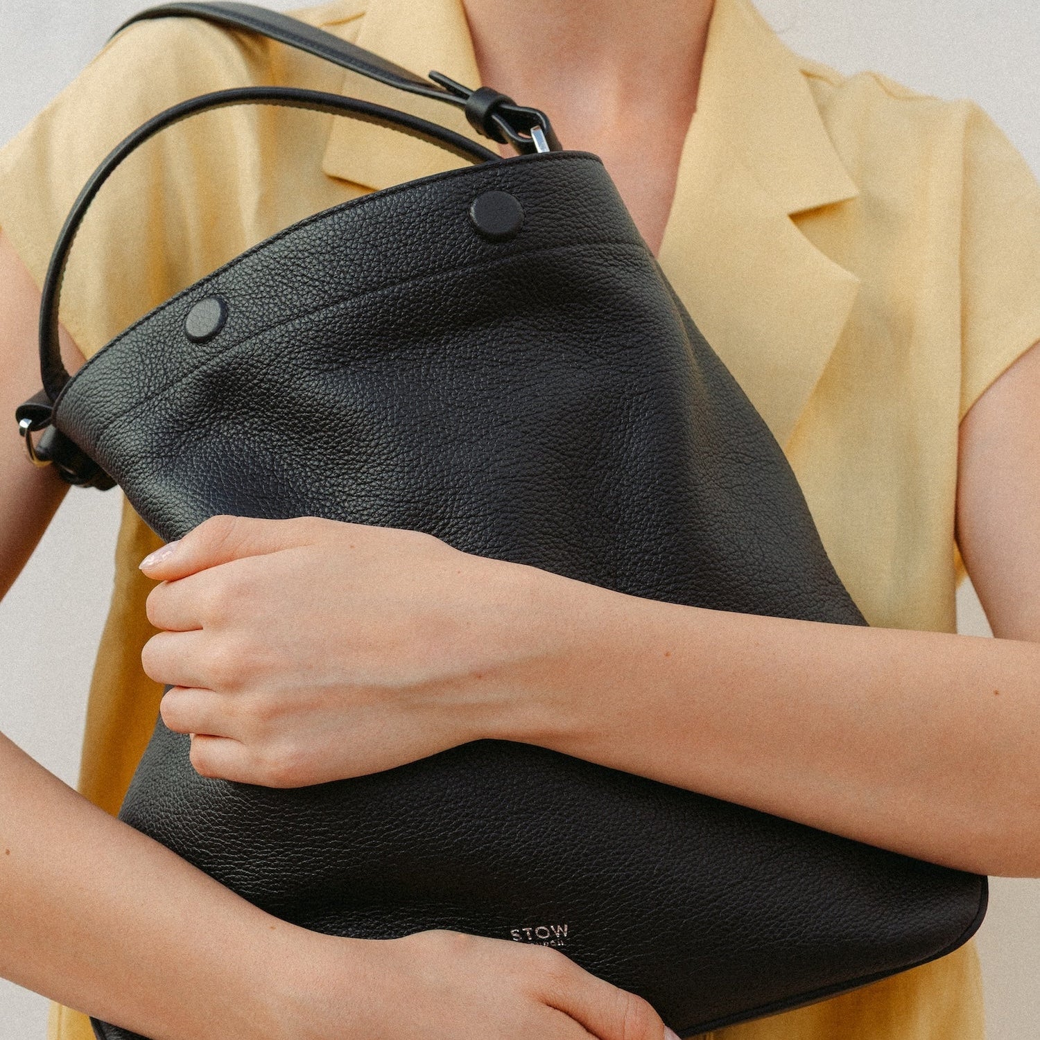 Model holding STOW London's Curve in Black leather featuring the detachable shoulder strap and top handle with silver hardware and details