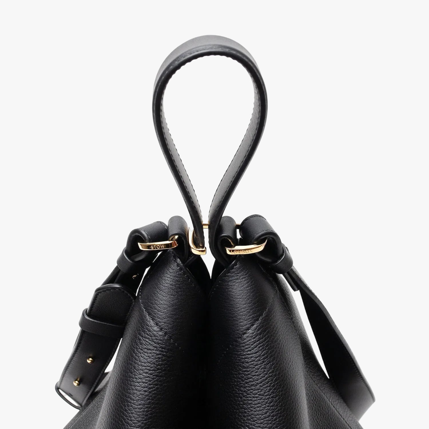 Close up of the handles on Stow London's Curve bag in Black pebbled leather featuring gold-coated stainless steel hardware and clip and detachable strap on a light grey background