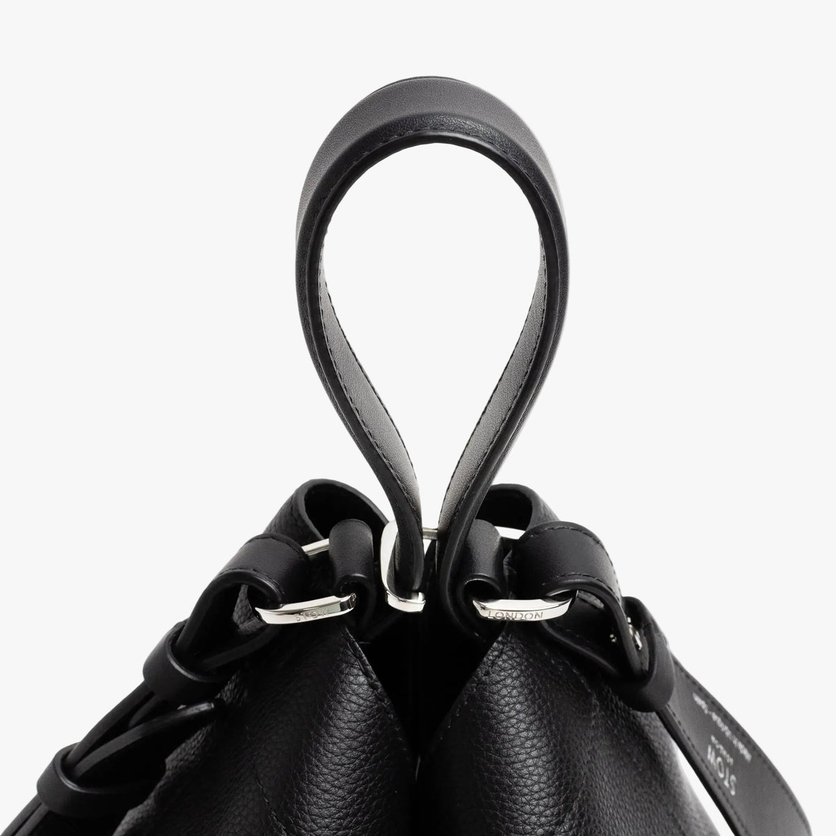 Close up of the handles on Stow London's Curve bag in Black pebbled leather featuring silver stainless steel hardware and clip and detachable strap on a light grey background