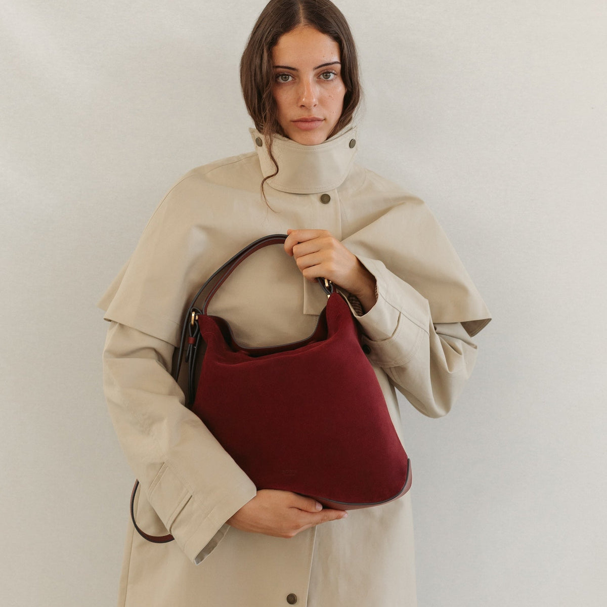 Model in a trench coat with STOW London's Curve bag in Burgundy Suede leather featuring the detachable crossbody strap