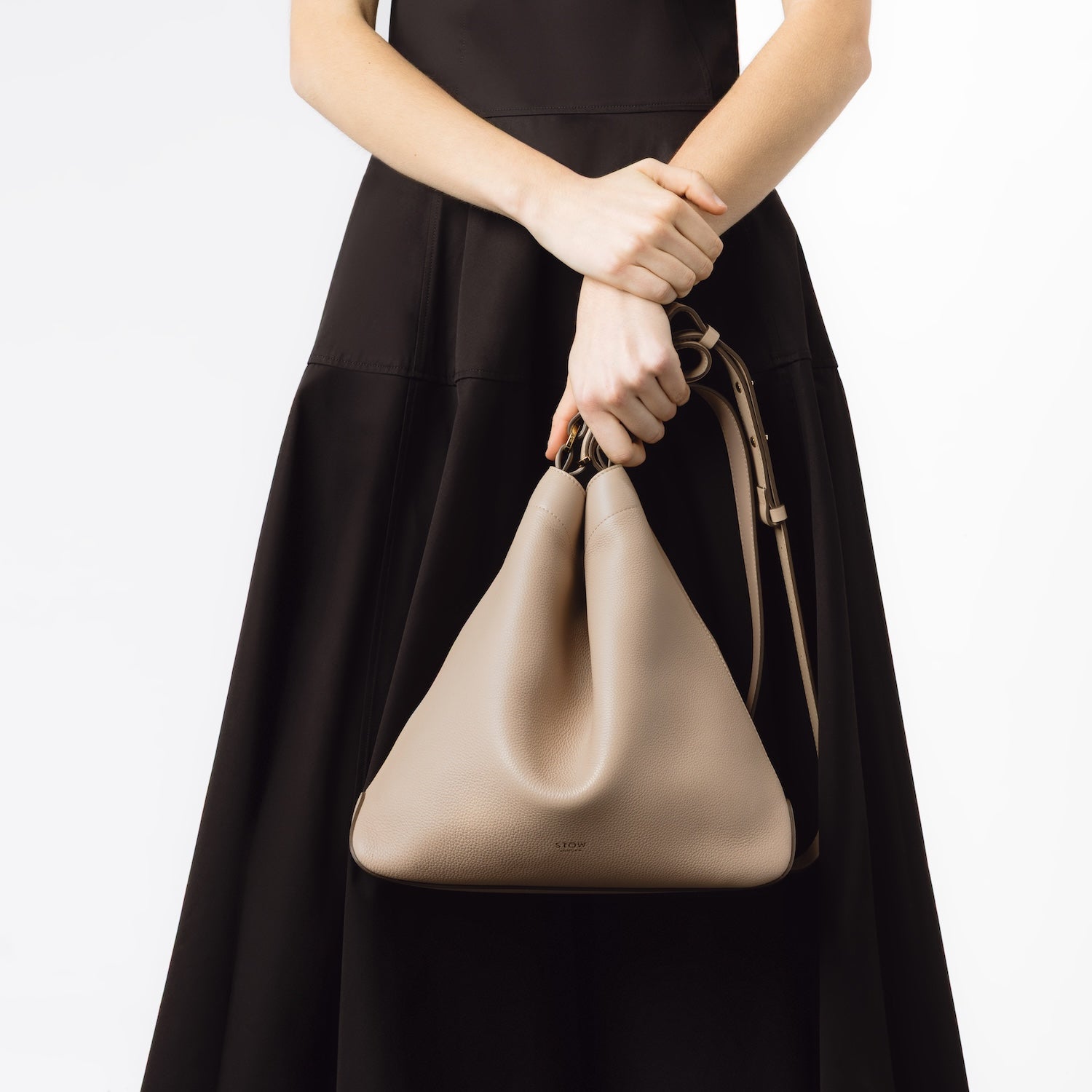Model holding STOW London's Curve bag in Camel pebbled leather by the handle at her front on a white background