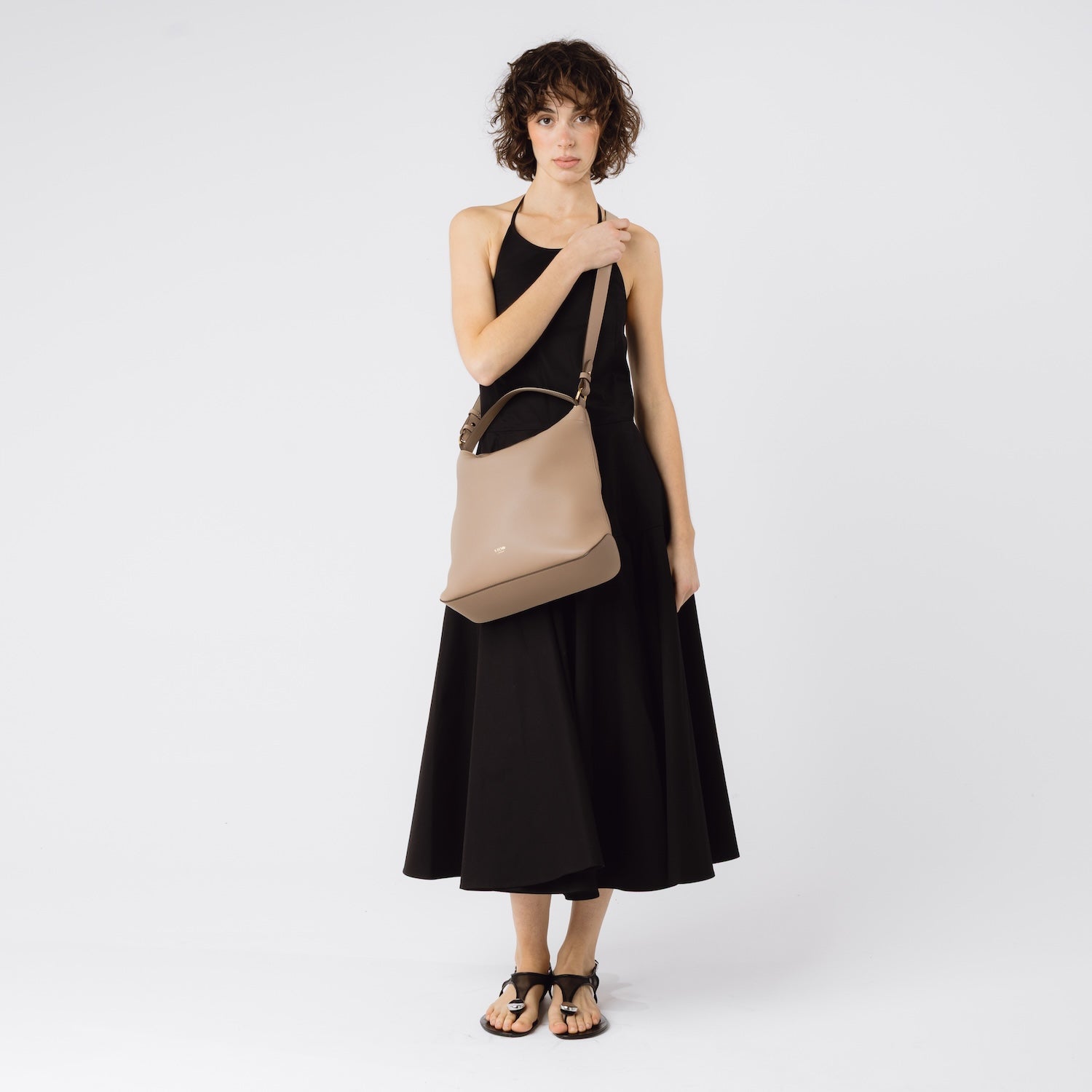 Model wearing STOW London's Curve bag in Camel pebbled leather crossbody featuring gold-coated stainless steel hardware on a white background