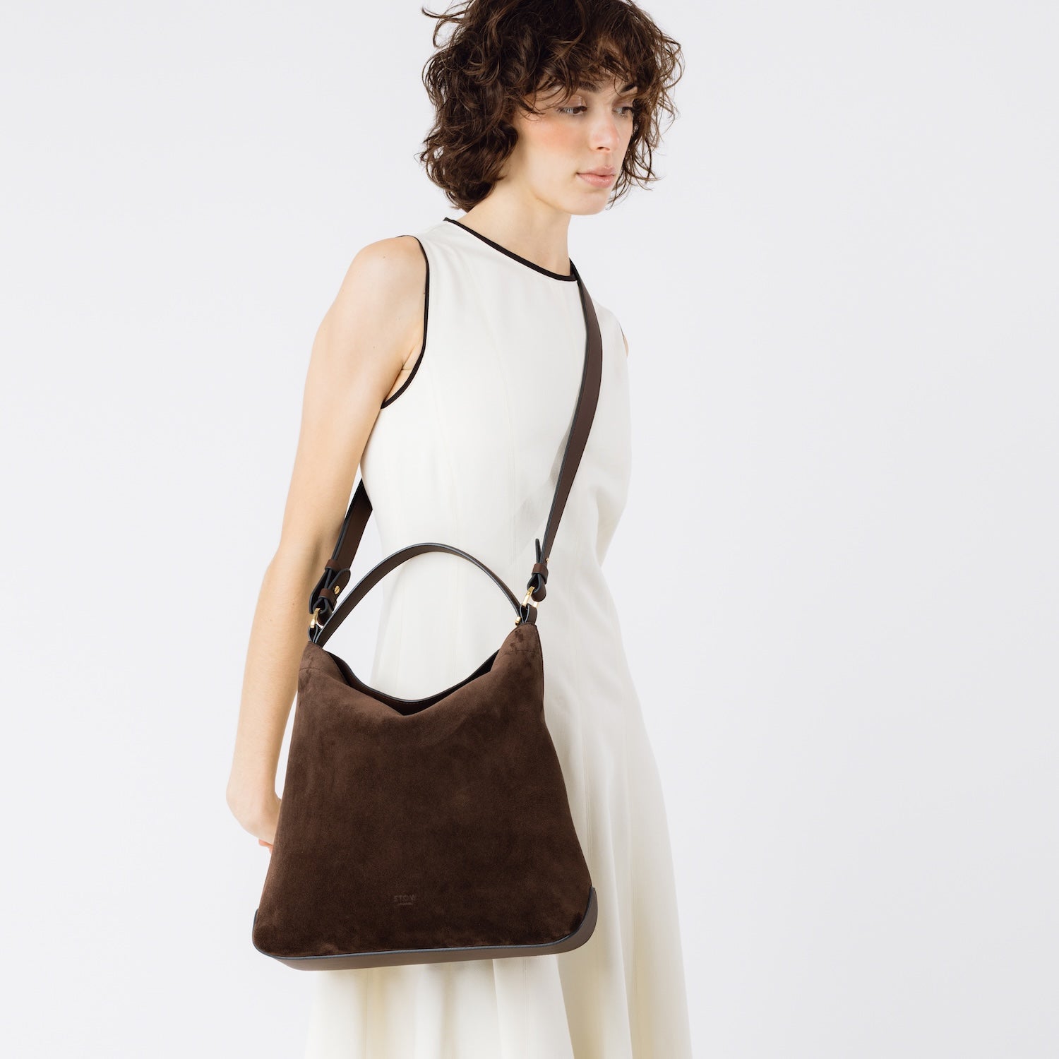 Model wearing STOW London's Curve bag in Chocolate suede leather crossbody featuring gold-coated stainless steel hardware