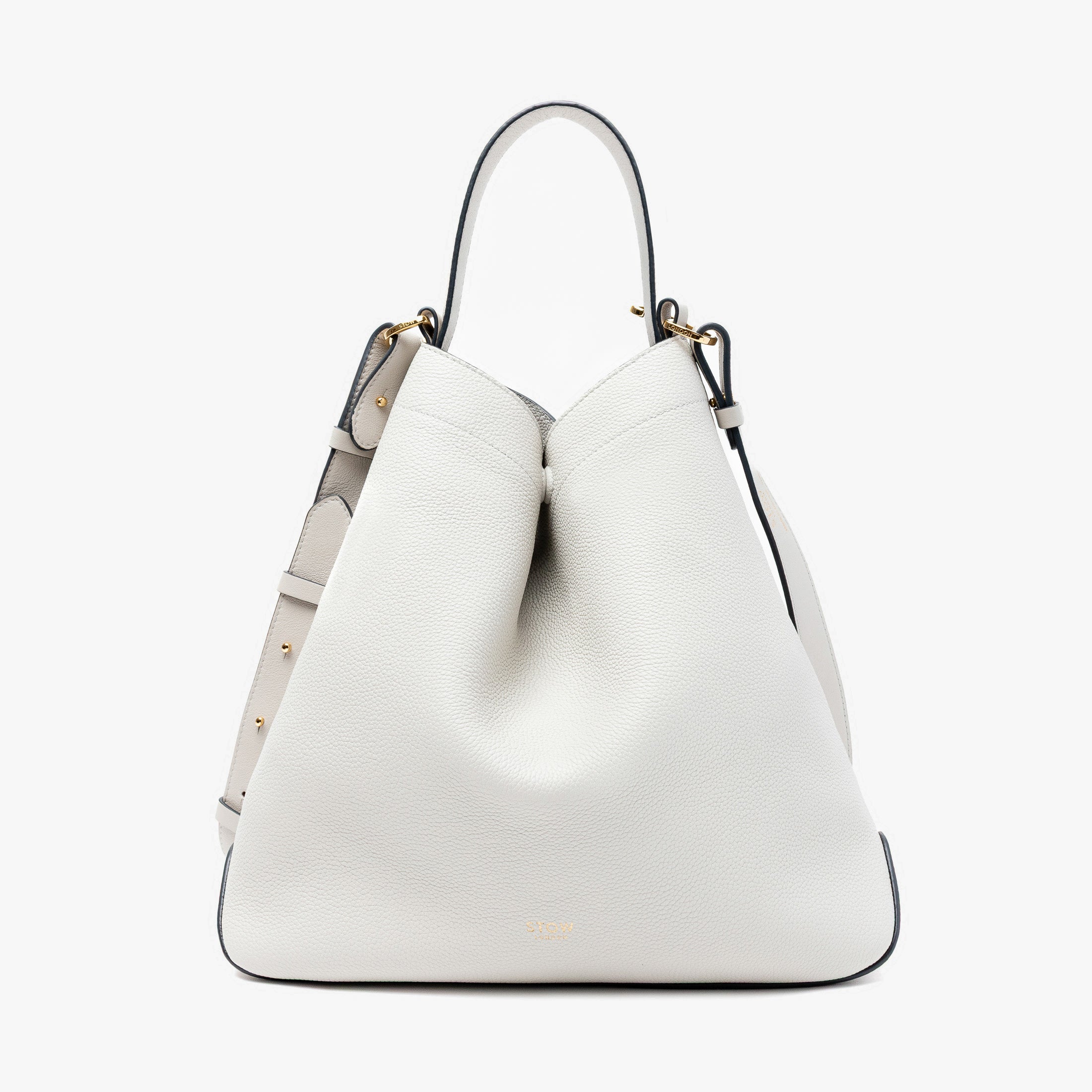 Stow London's Curve bag in Cloud Grey pebbled leather shaped in a triangular form featuring gold-coated stainless steel hardware on a light grey background