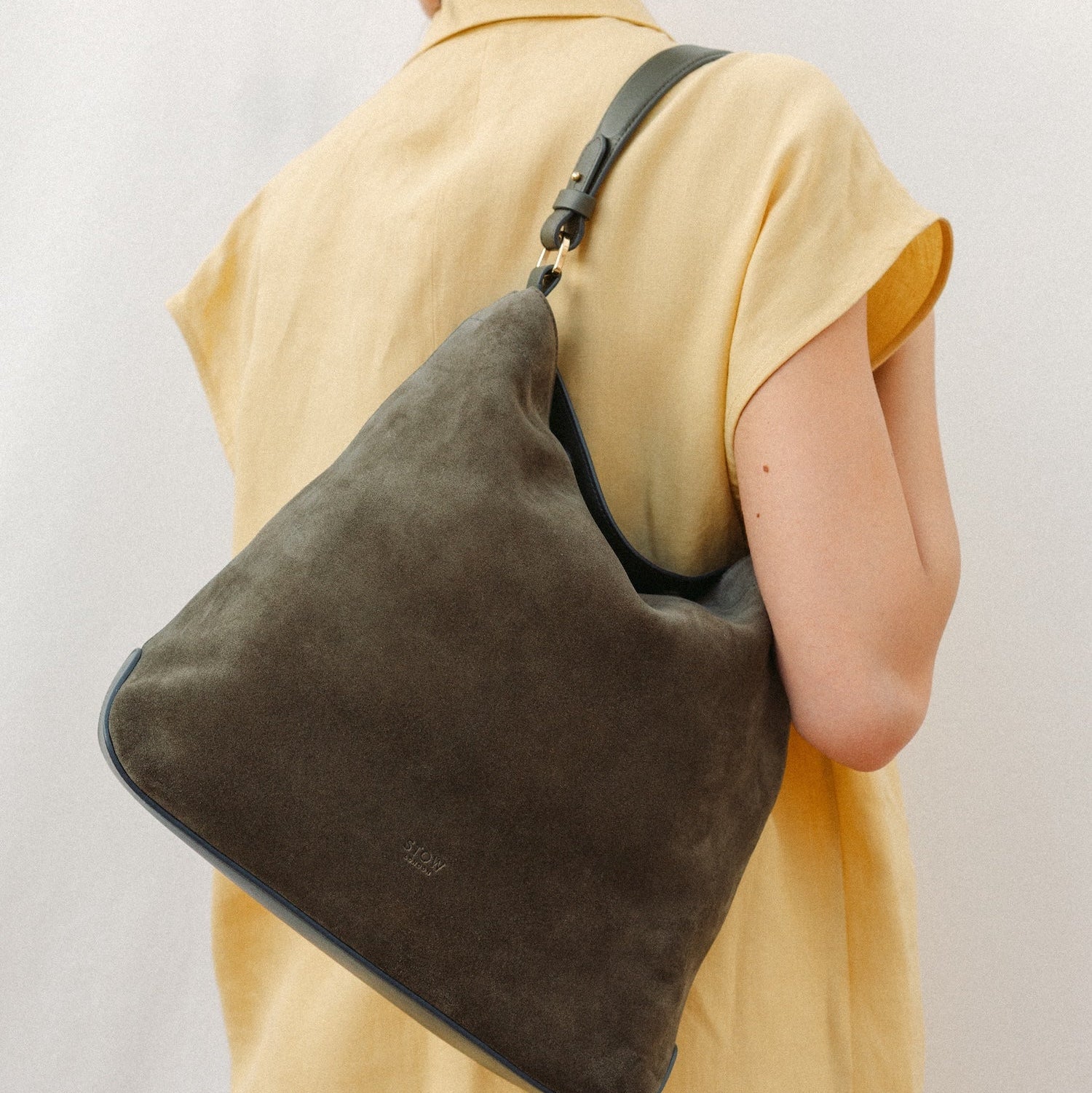 Model wearing STOW London's Curve in Dark Green suede featuring the detachable shoulder strap with gold hardware