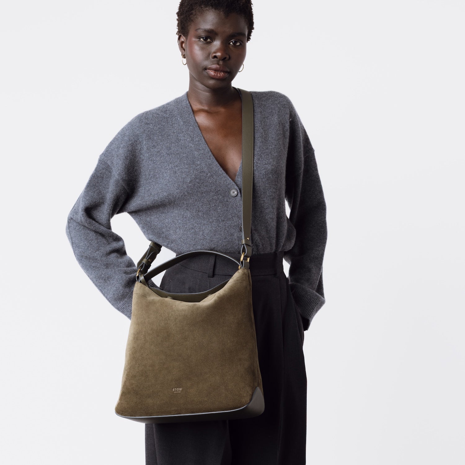 Model wearing Stow London's Curve bag in Dark Green suede leather crossbody featuring gold-coated stainless steel hardware on a white background