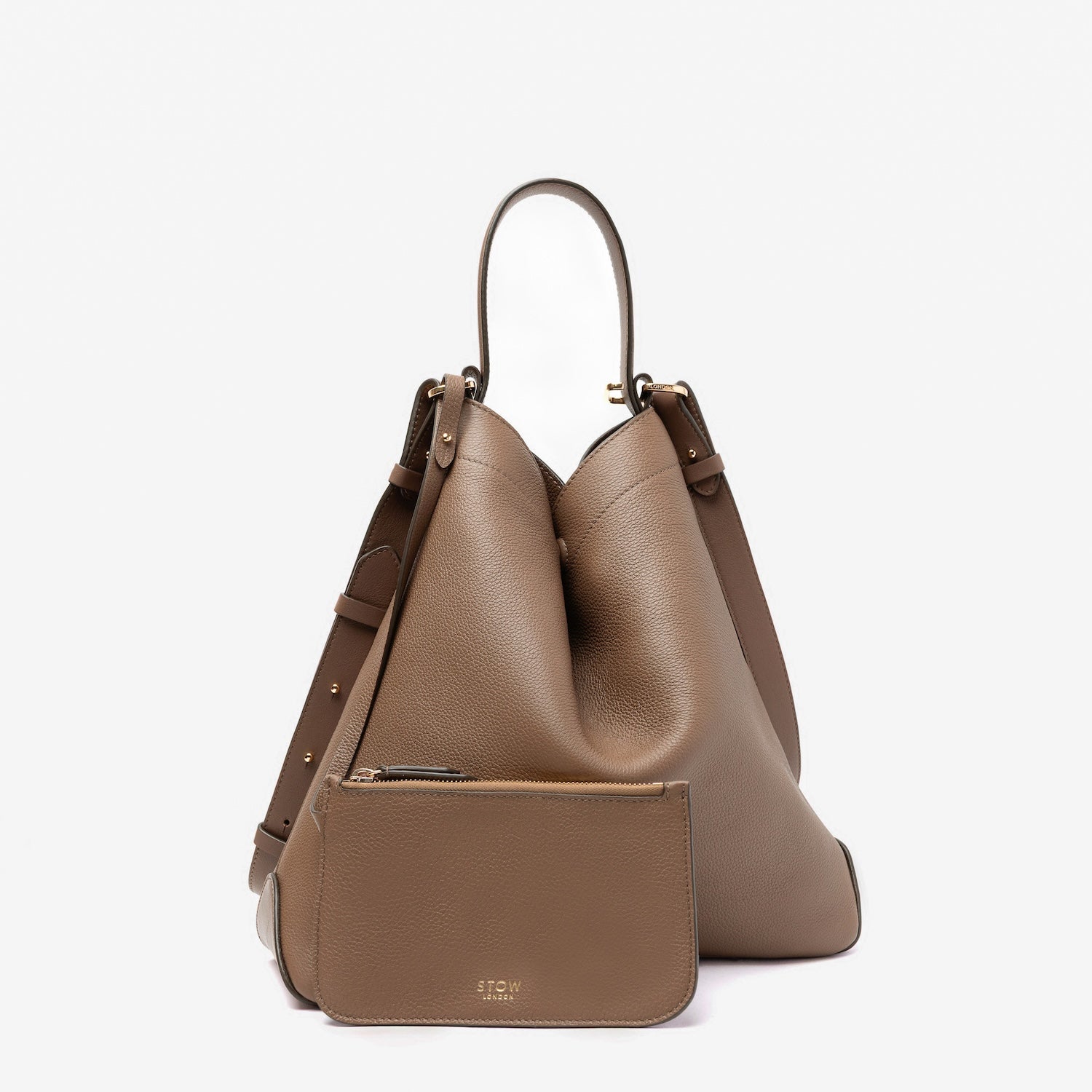 STOW London's Curve bag in Mocha pebbled leather styled in its triangular form featuring its matching interior pouch and gold-coated stainless steel hardware on a light grey background
