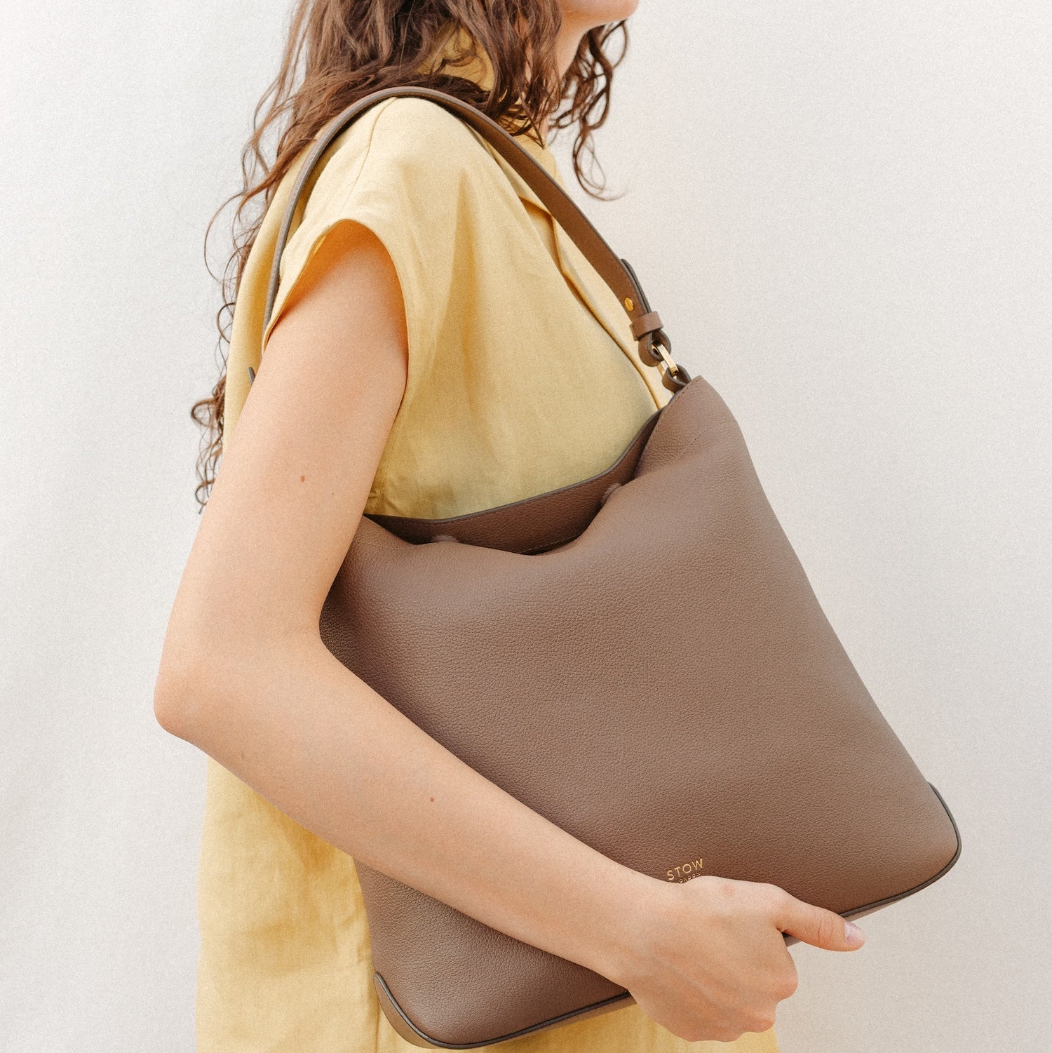 Model wearing STOW London's Curve in Mocha leather featuring the detachable shoulder strap with gold hardware and details