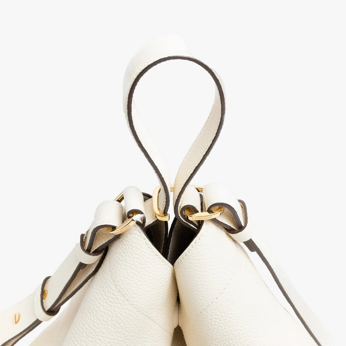 Close up of the handles on STOW London's Curve bag in Spring Moon pebbled leather featuring gold-coated stainless steel hardware and clip and detachable strap on a light grey background