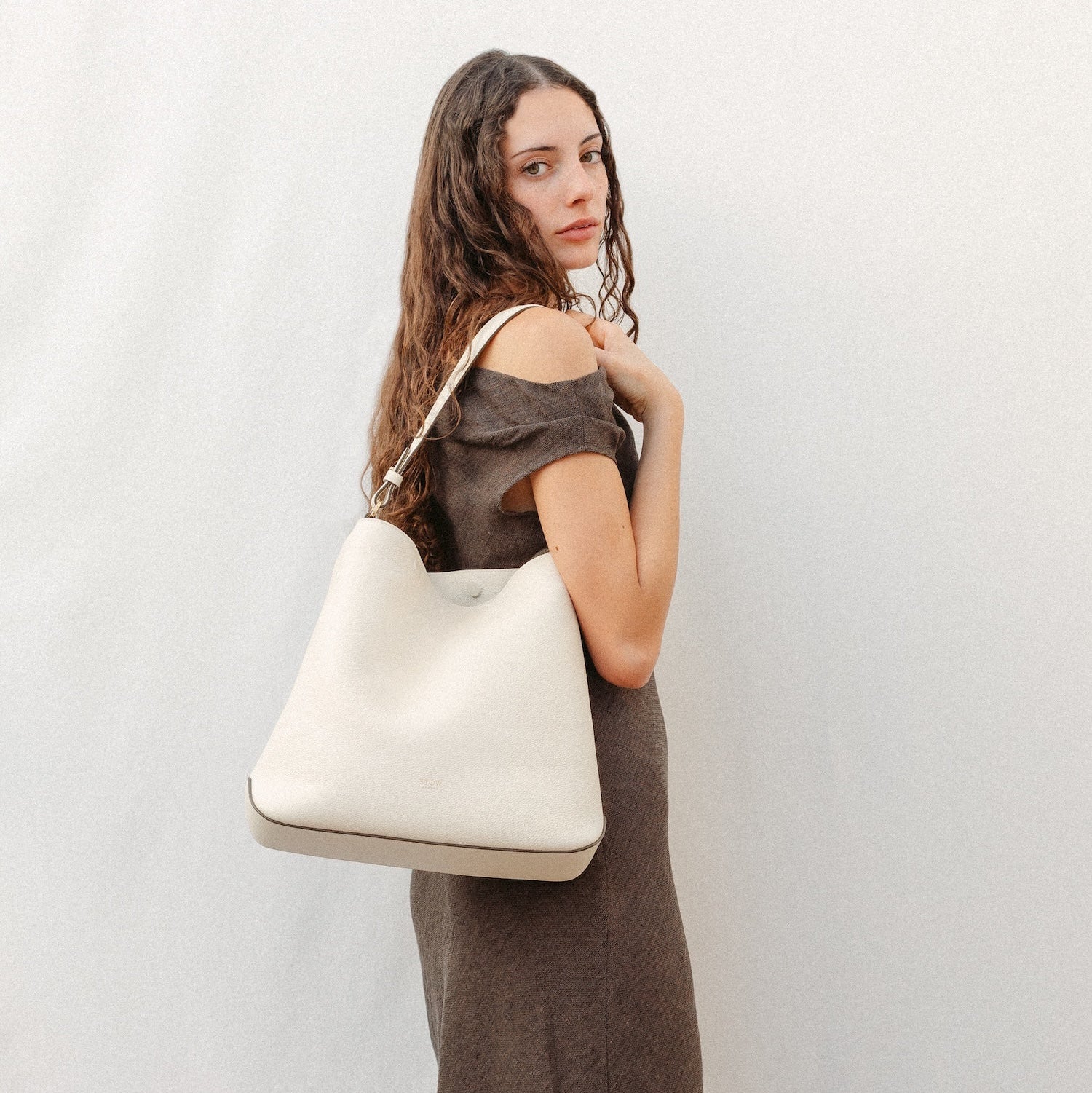 Model wearing STOW London's Curve in Spring Moon leather featuring the detachable shoulder strap with gold hardware and details