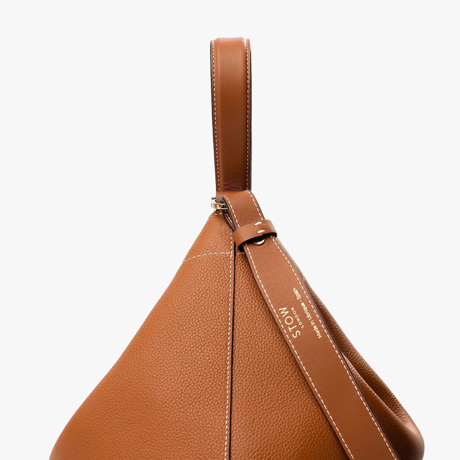 Side view of Stow London's Curve bag in Earth Tan pebbled leather featuring gold-coated stainless steel hardware on a light grey background