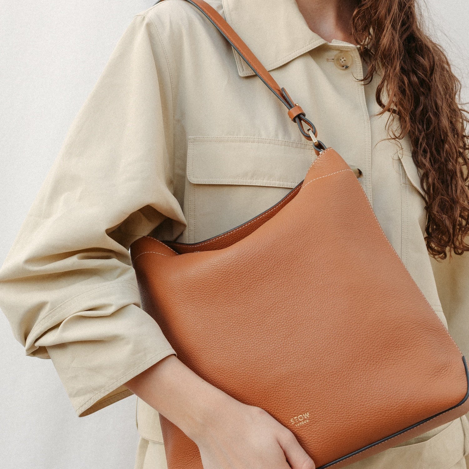 Model wearing STOW London's Curve in Earth Tan leather featuring the detachable shoulder strap with gold hardware and details