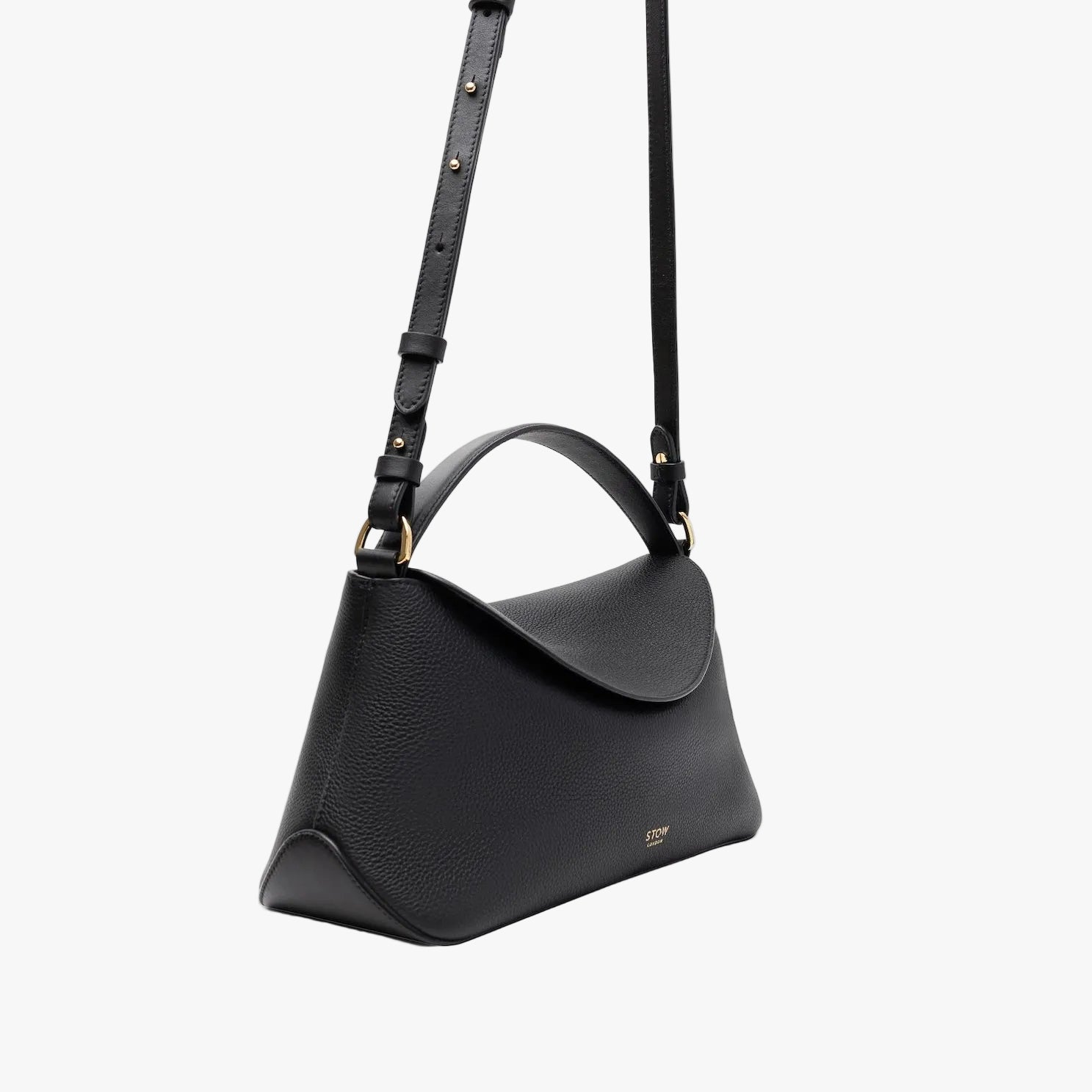 Off-axis view of STOW London's East West in Black pebbled leather and detachable crossbody strap featuring gold-coated stainless steel hardware on a light grey background