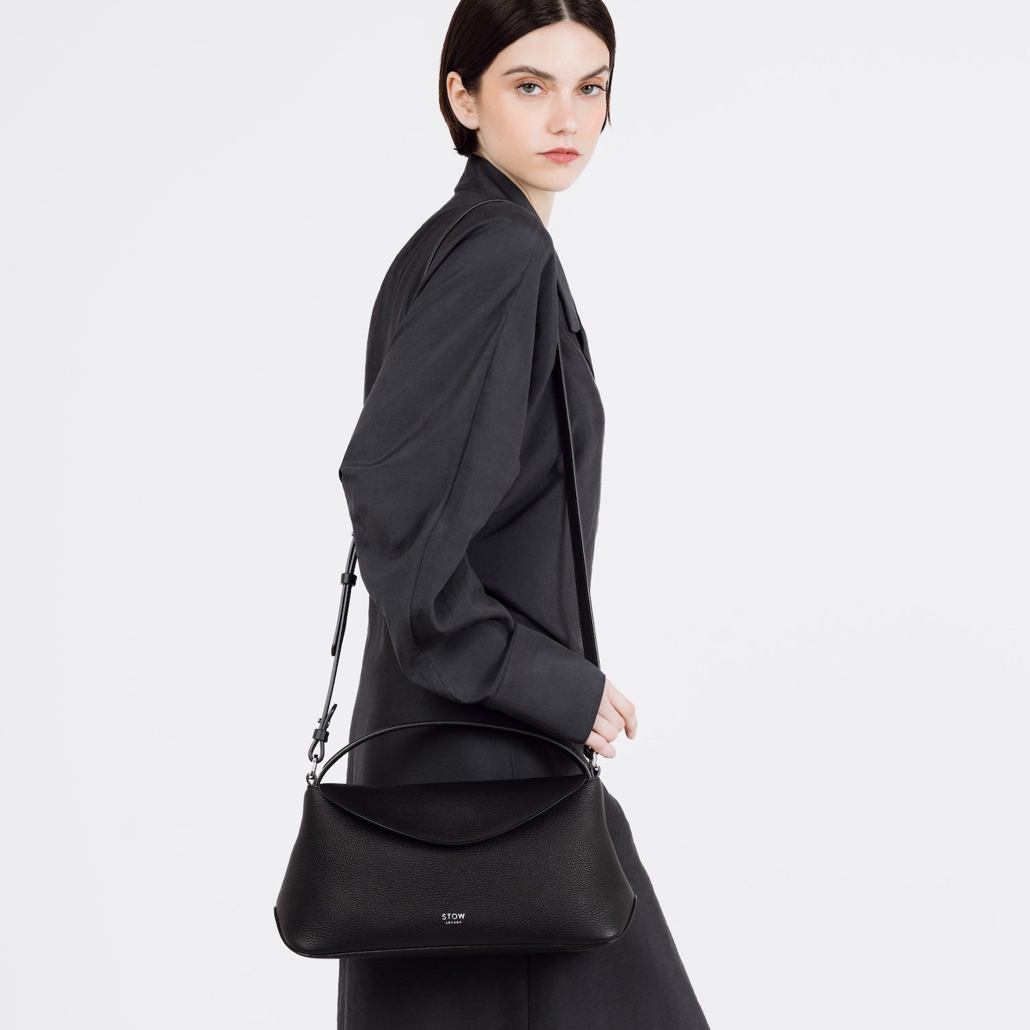 Model wearing STOW London's East West bag in Black pebbled and smooth leather on her shoulder featuring silver stainless steel hardware on a white background