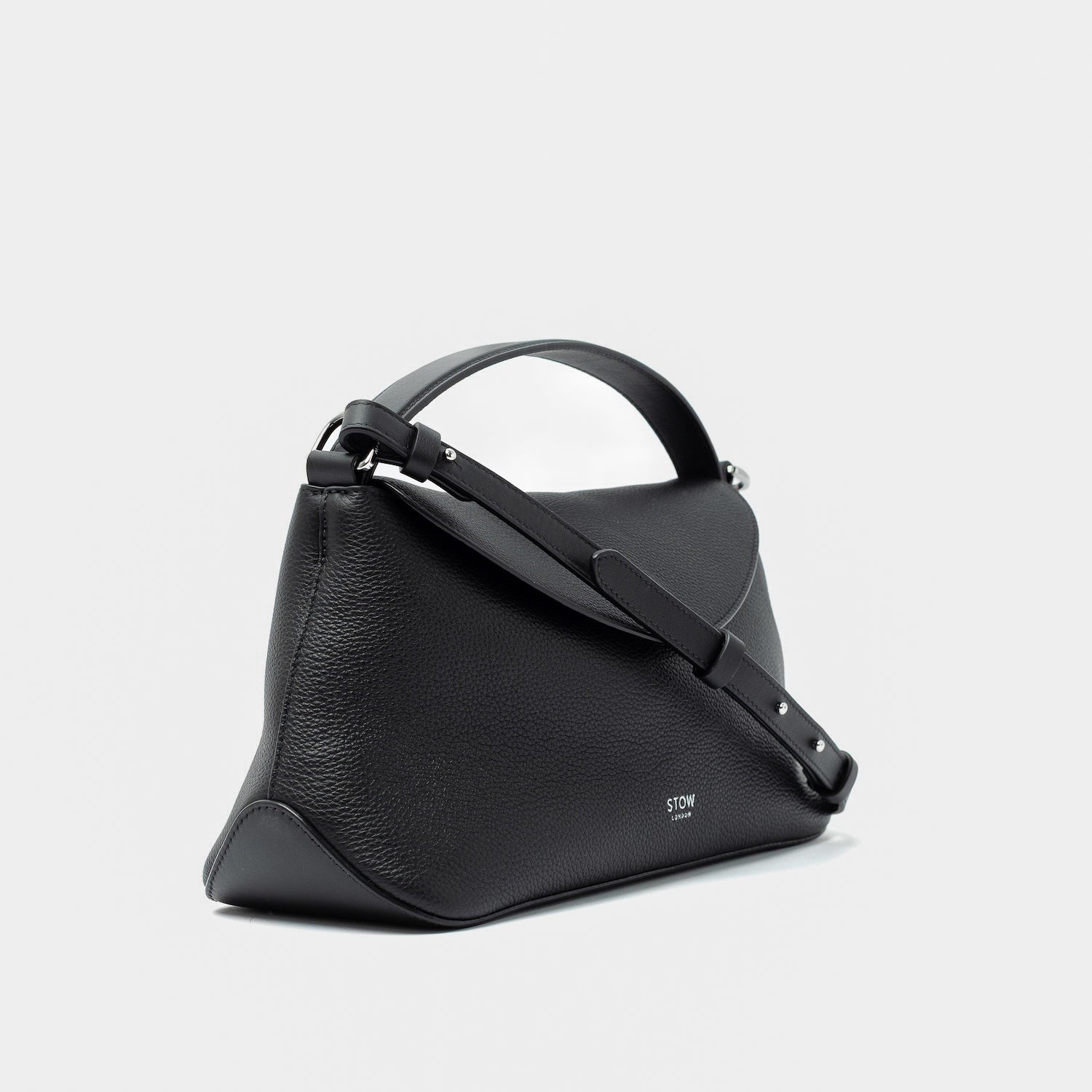 Side view of STOW London's East West in Black pebbled leather and detachable crossbody strap featuring silver stainless steel hardware on a light grey background