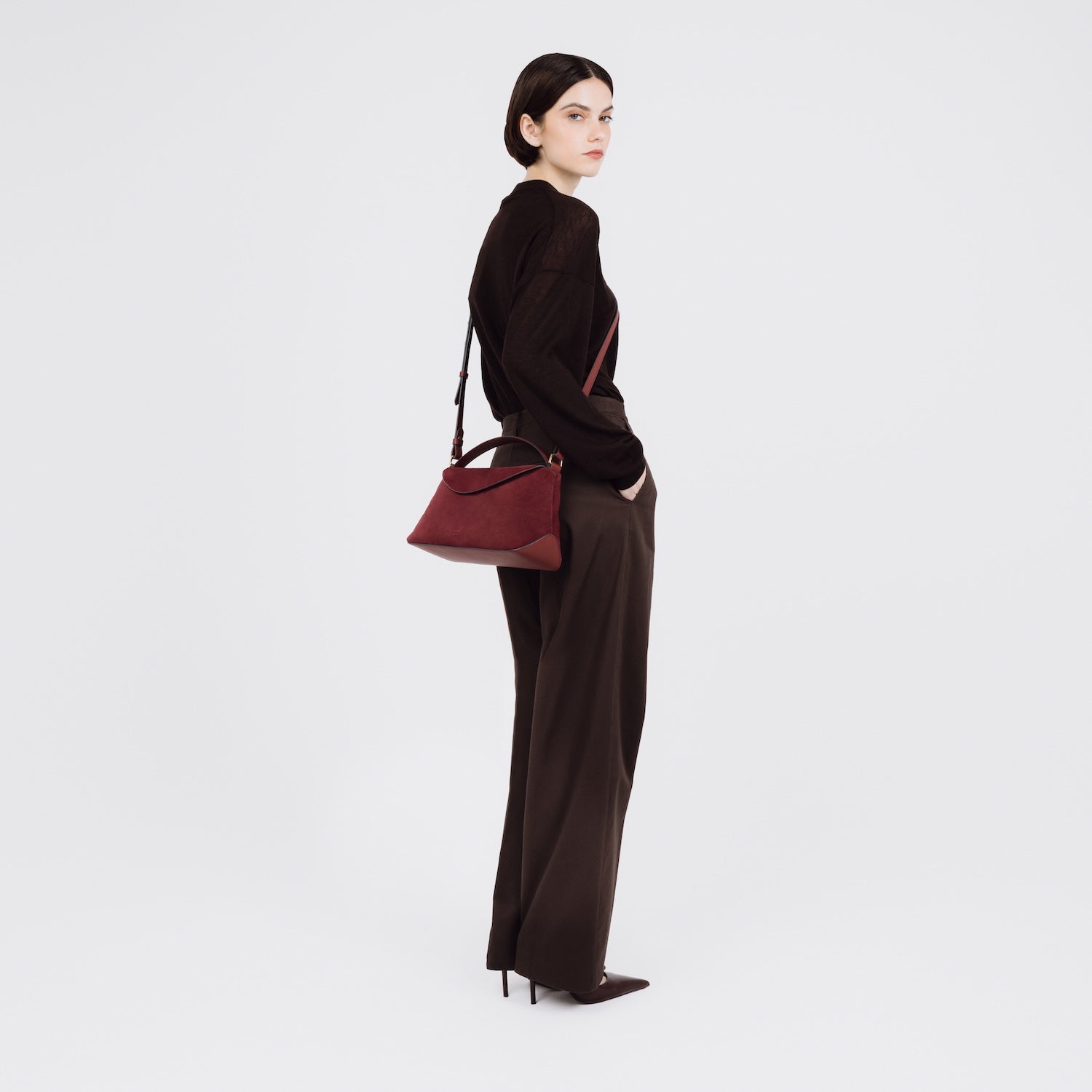 Model wearing STOW London's East West bag in Burgundy Suede leather crossbody featuring gold-coated stainless steel hardware on a white background